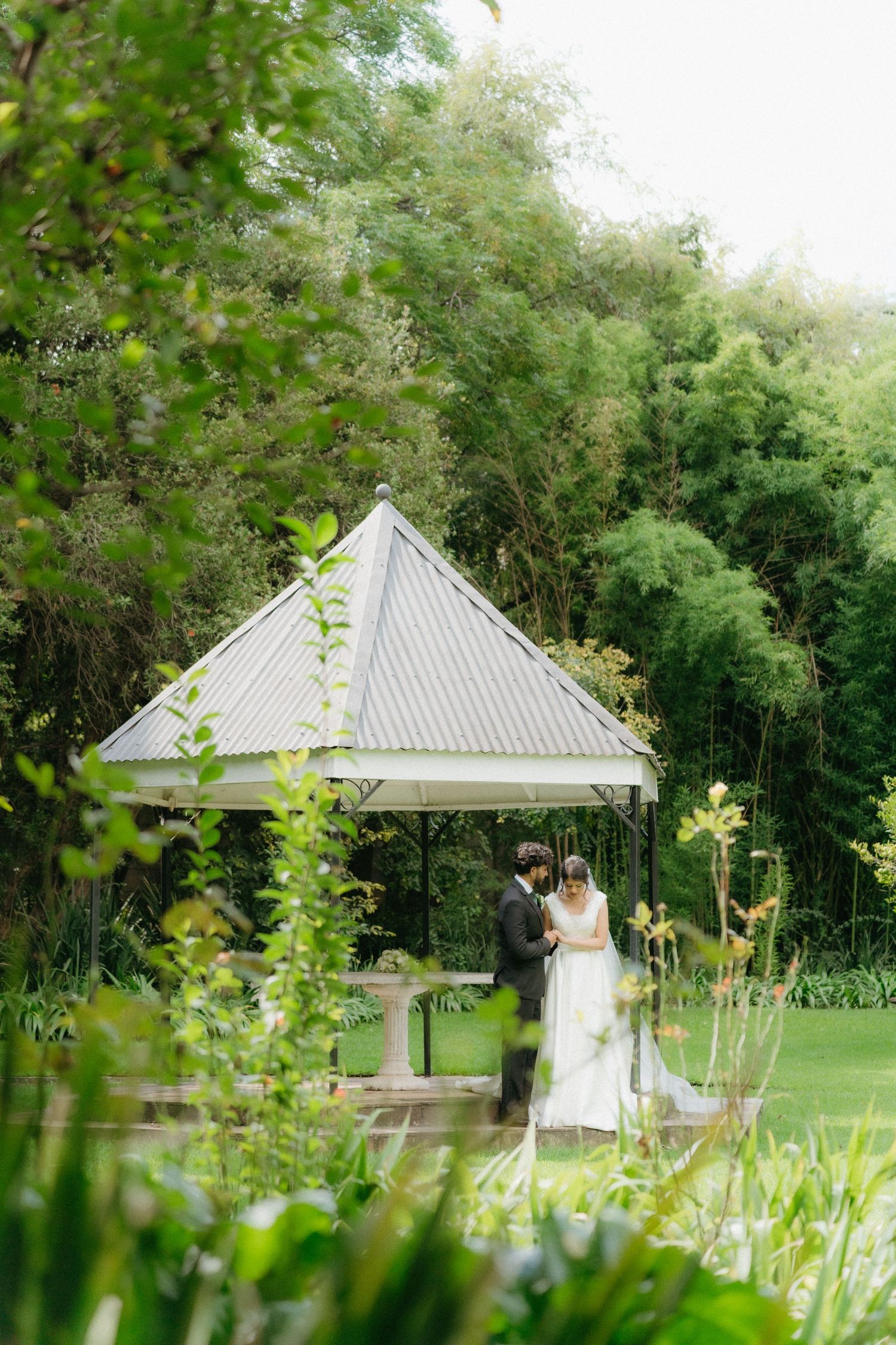 A white gazebo surrounded by lush greenery provides an intimate wedding ceremony setting.