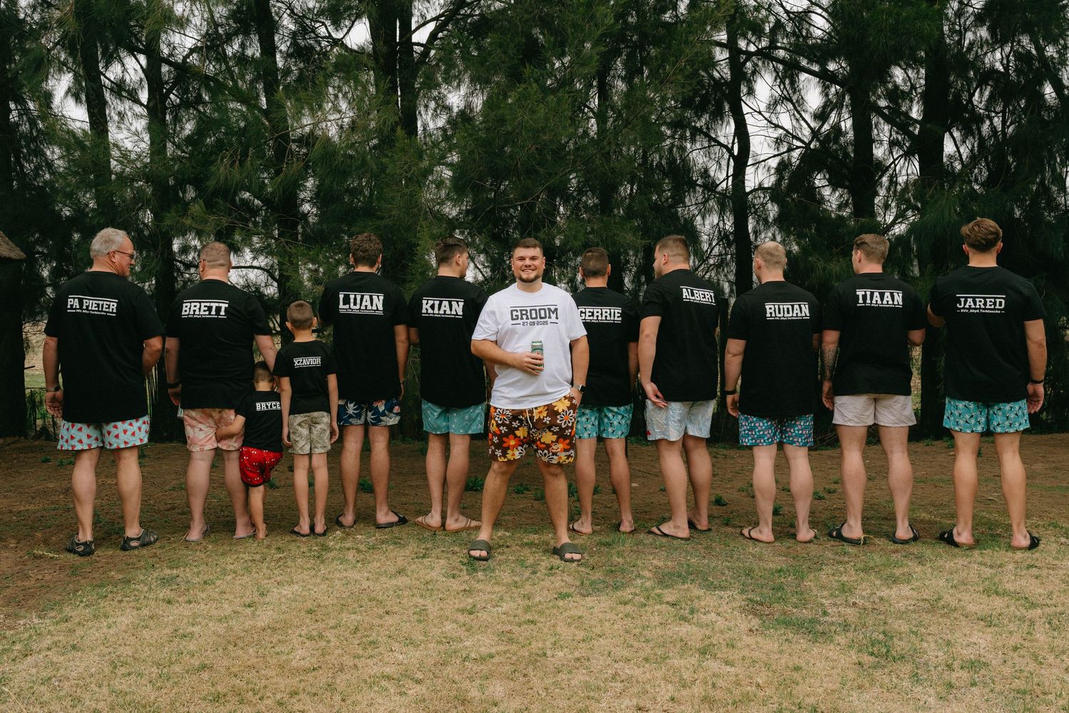 Wedding party members lined up showing their shorts in a fun outdoor photo.