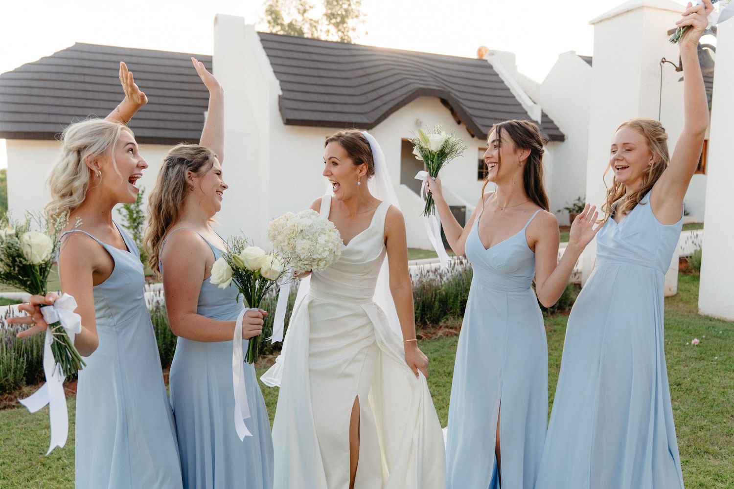 Bridesmaids in light blue dresses dance and celebrate at an outdoor wedding reception.