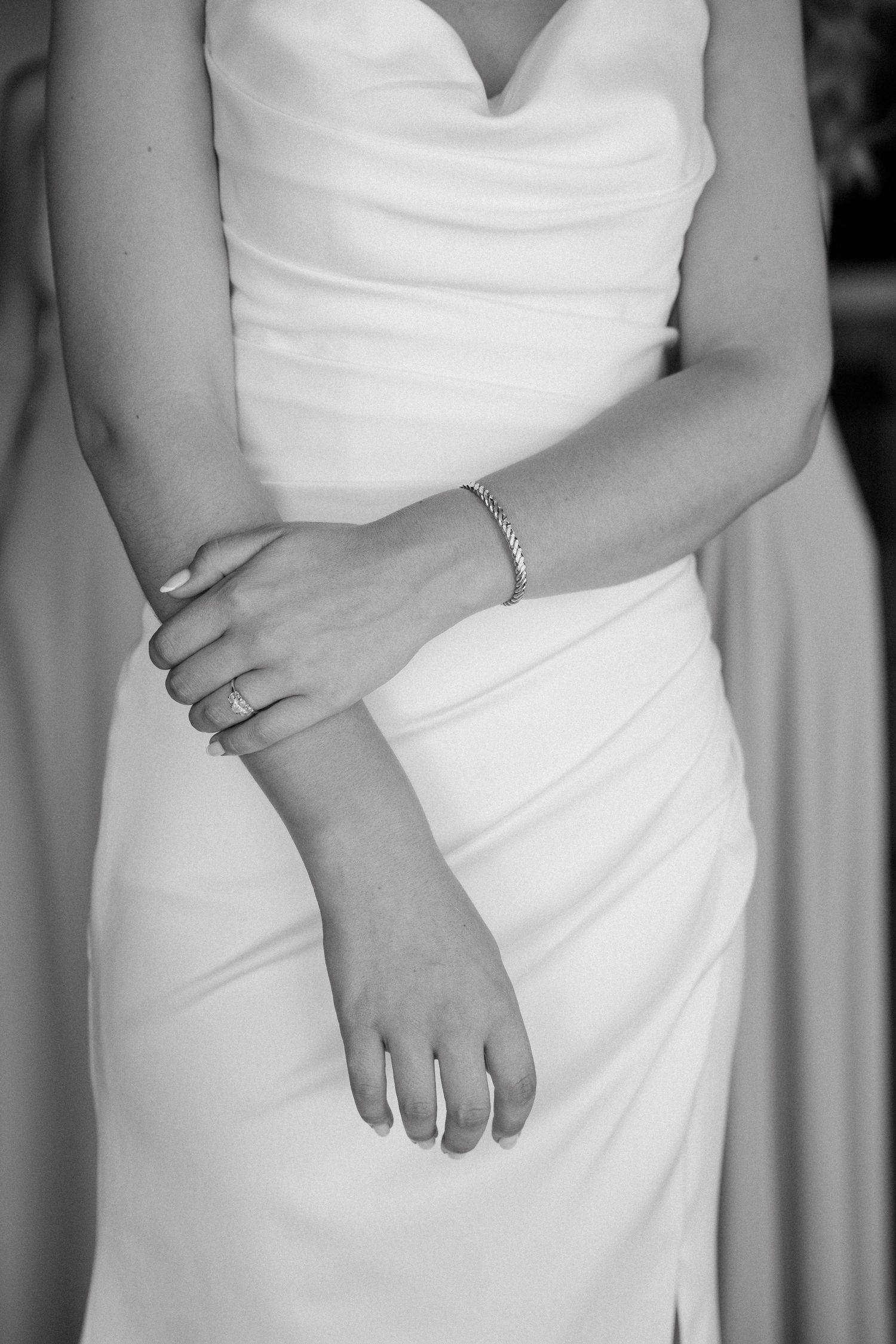 Black and white close-up details of an elegant strapless white wedding dress showing pleated fabric draping and texture.