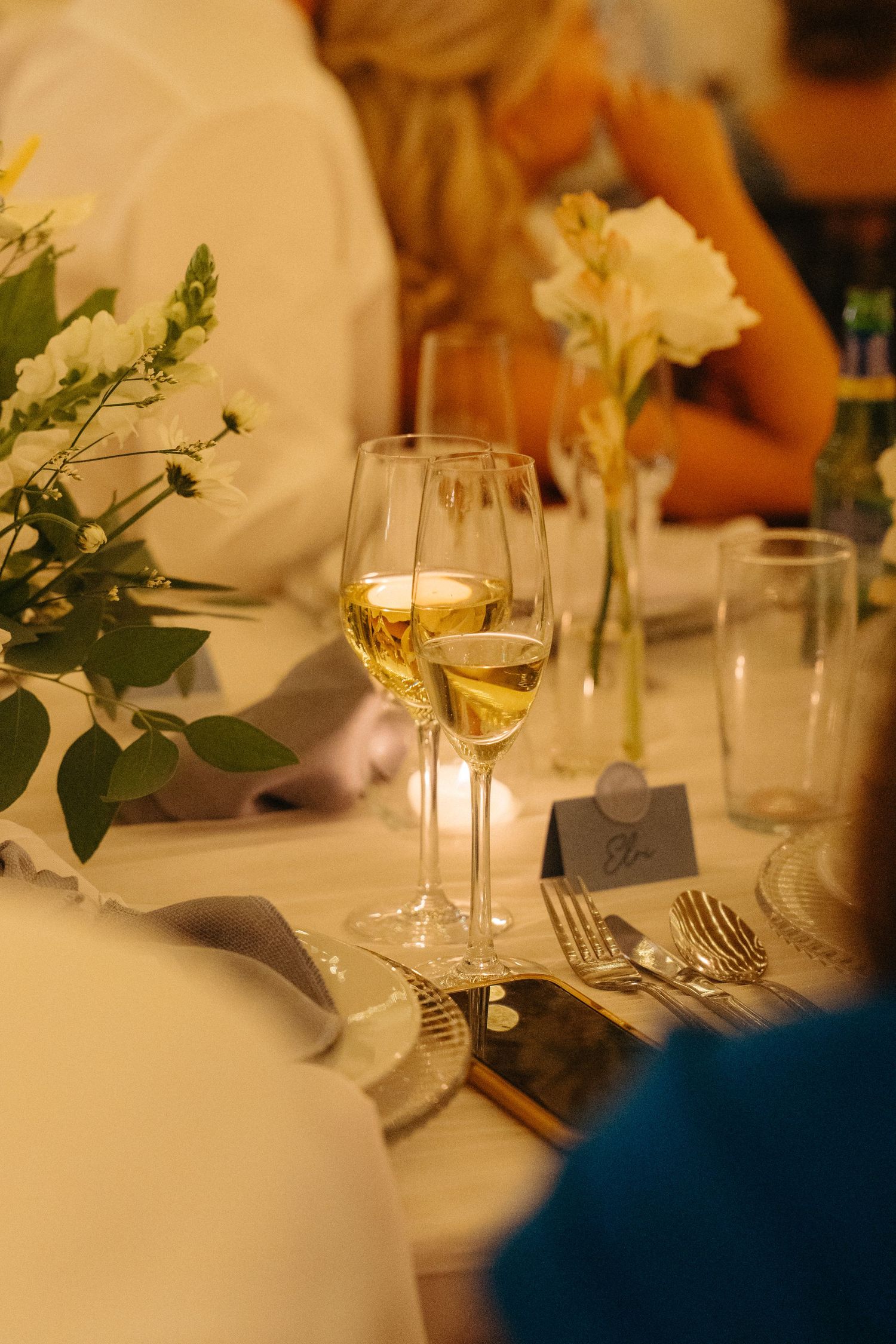 Elegant wedding reception table settings with white linens, floral centerpieces, and glowing candles in glass holders.
