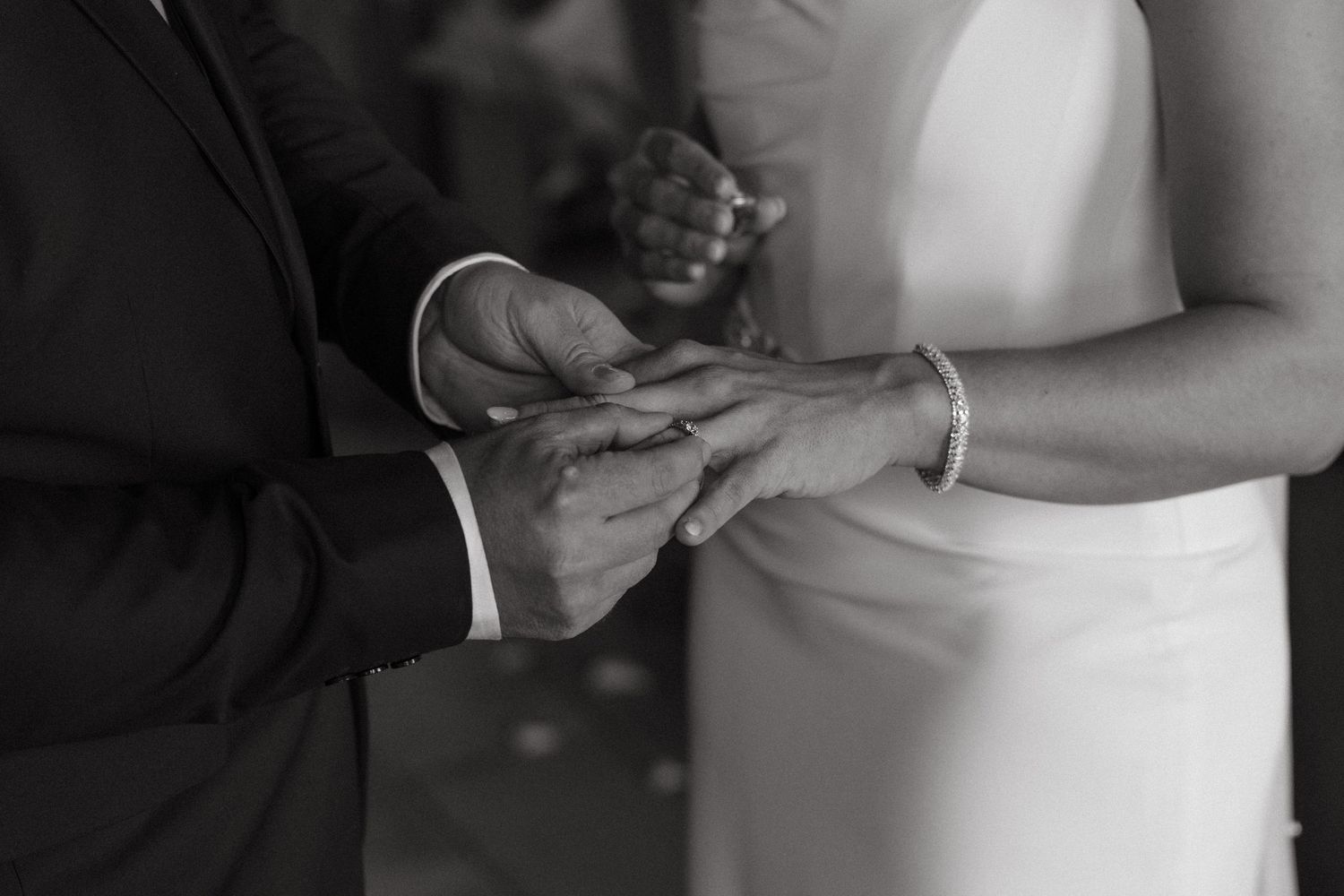 Black and white close-up of groom placing wedding ring on brides hand during ceremony. at La La Nathi, Harrismith