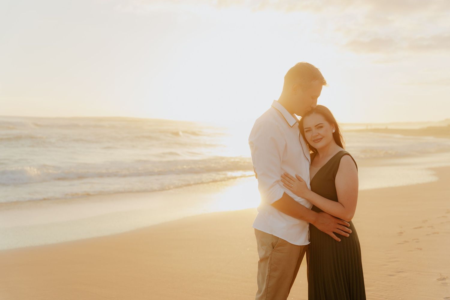 Romantic couple embracing on sandy beach near Mossel Bay at golden sunset with ocean waves in background.