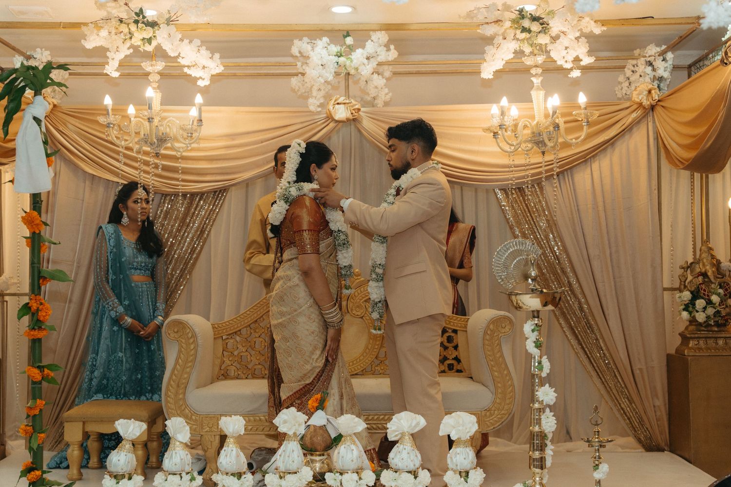 Elegant wedding reception venue with crystal chandeliers, white drapes, and ornate decor in a grand ballroom setting.