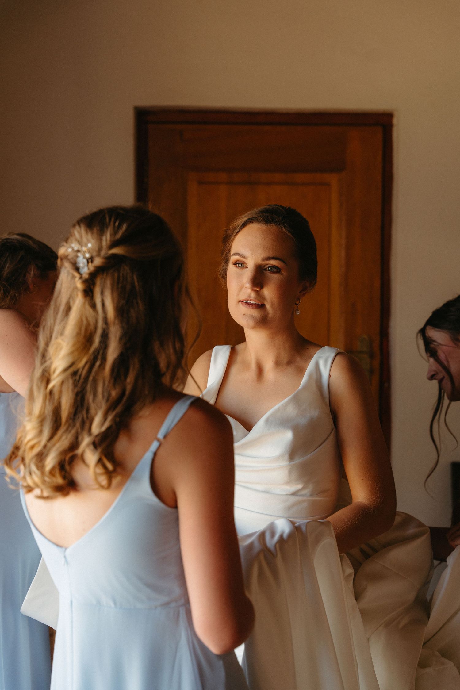 A group of people in formal attire gather in a warmly lit room with a wooden door in the background.