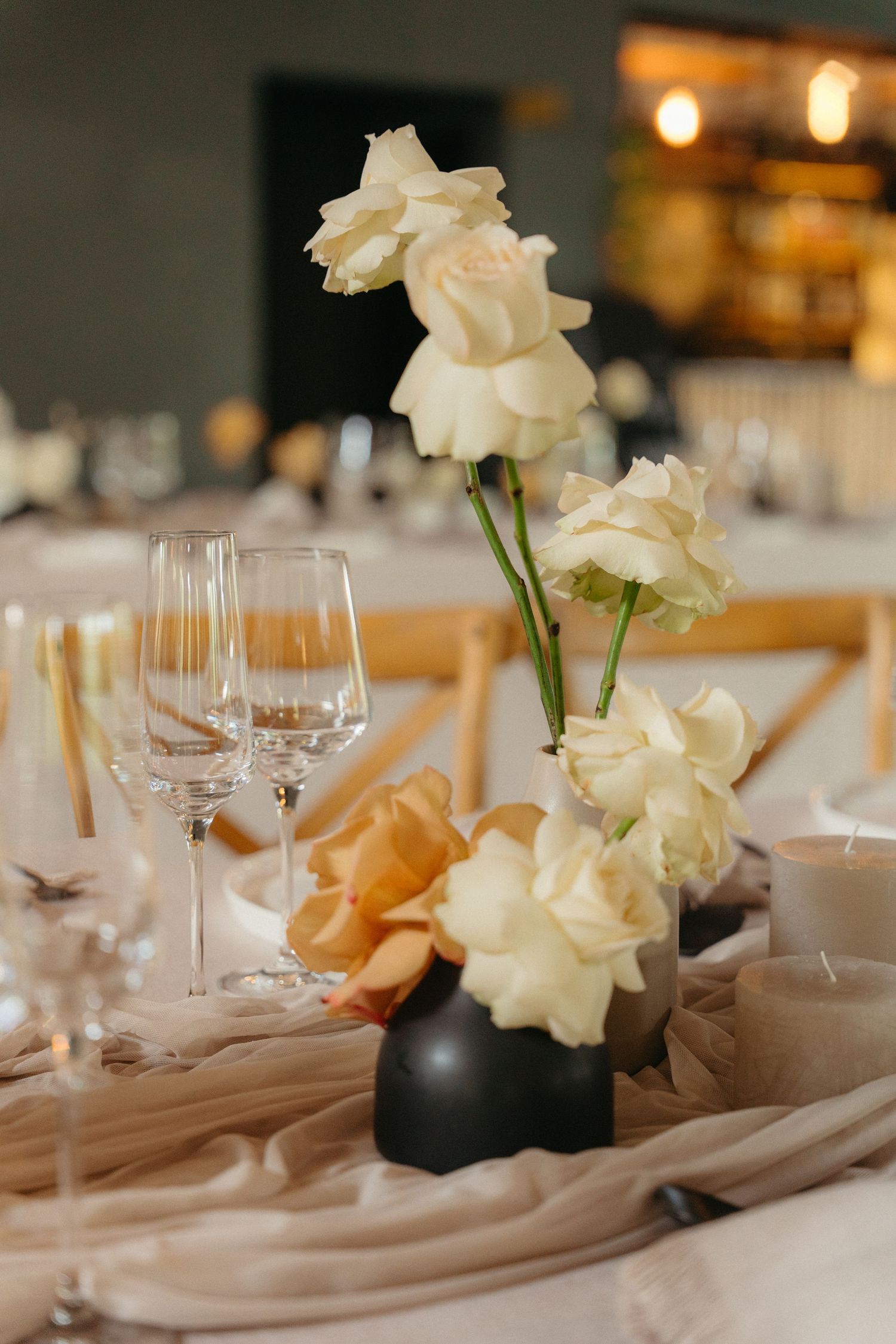Elegant table setting with white roses in black vases and wine glasses arranged in a row on neutral linens.