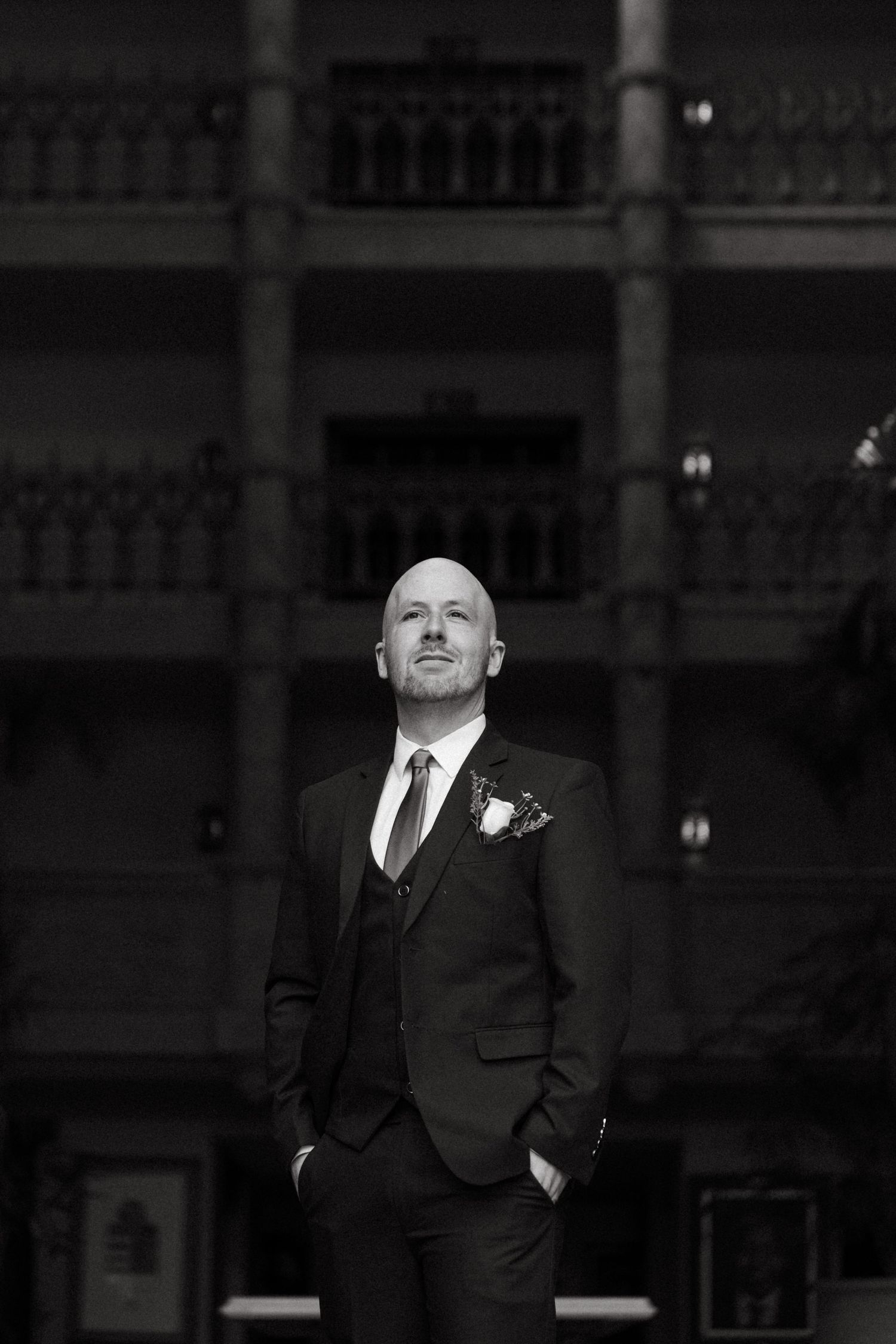 Bald groom in black suit with boutonniere stands confidently in The Palace of the Lost City, Sun City