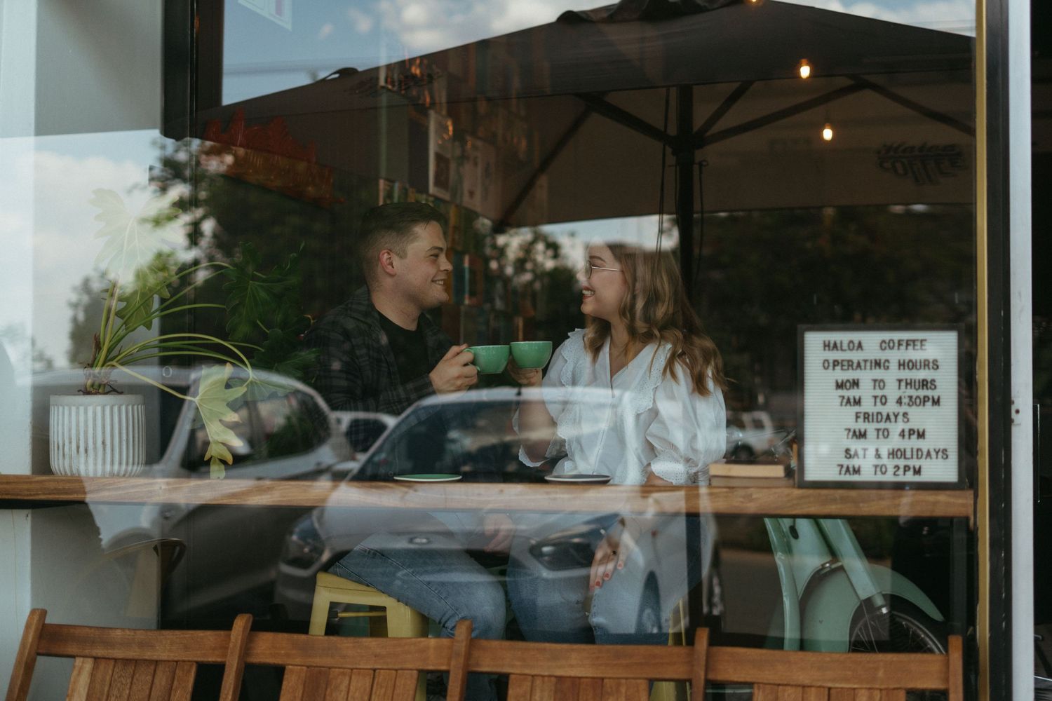 People enjoying conversation at a cafe table by a window with a large umbrella visible outside.