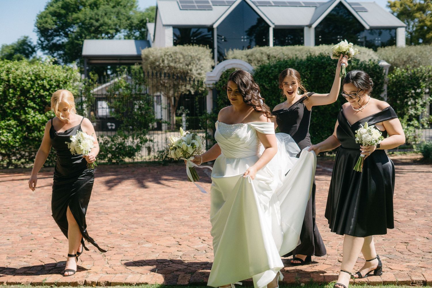 A group in formal attire dances together on a brick patio outside elegant blue buildings during a celebration.