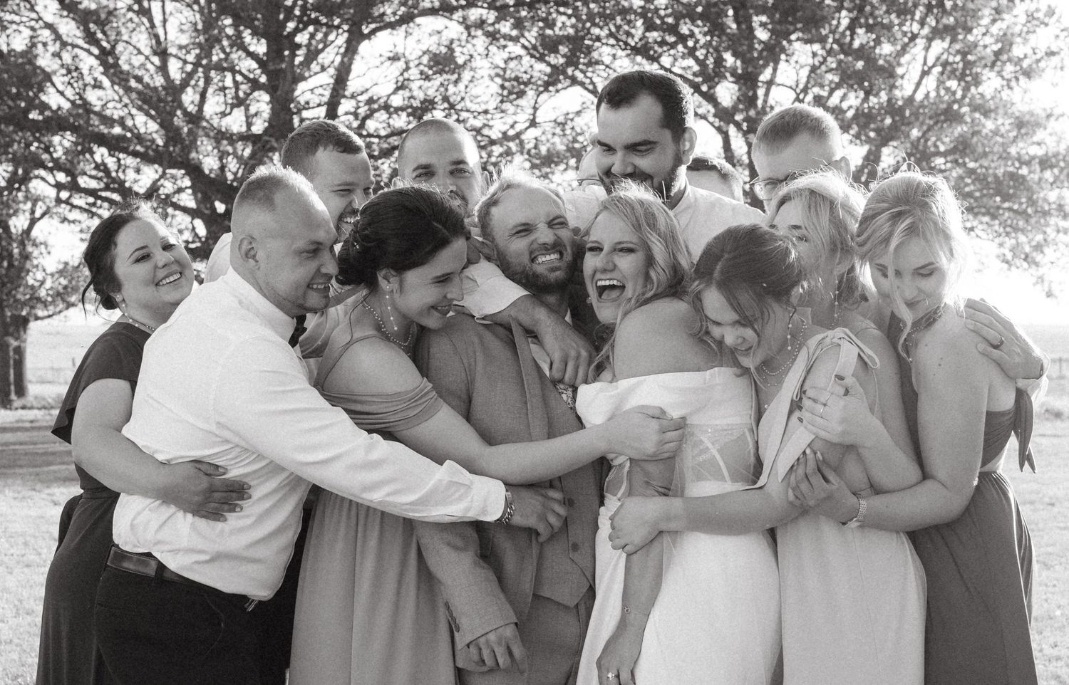Black and white photograph showing a group of people gathered closely together in a joyful embrace outdoors.
