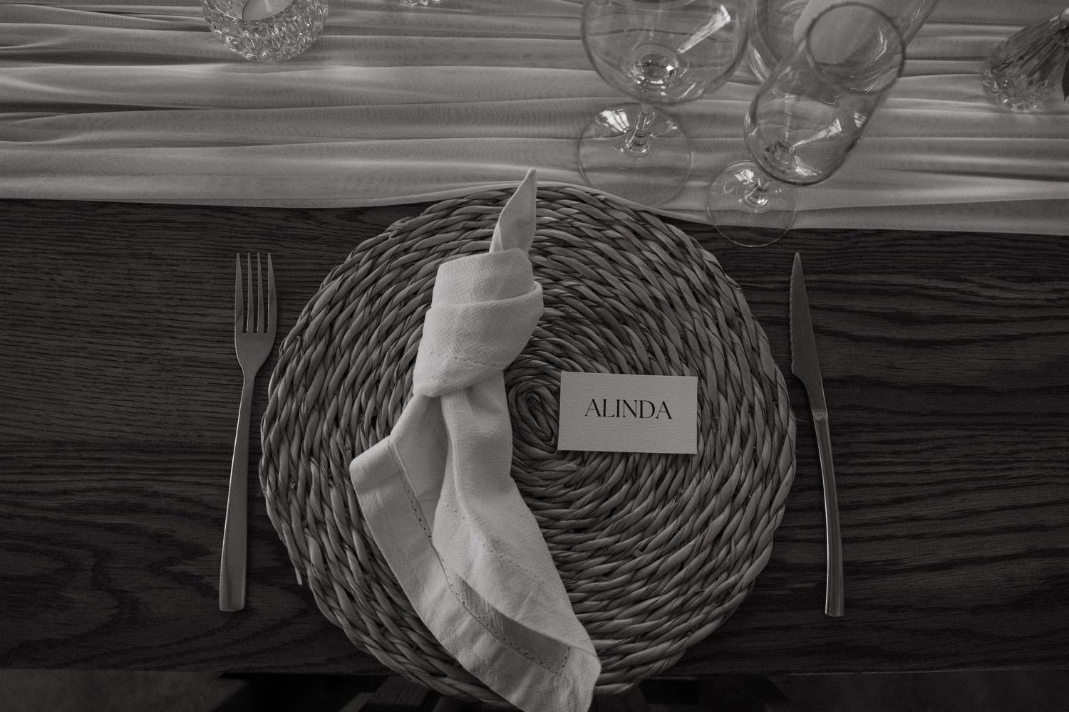 Black and white overhead view of table setting with circular woven placemat, napkin, and menu card.