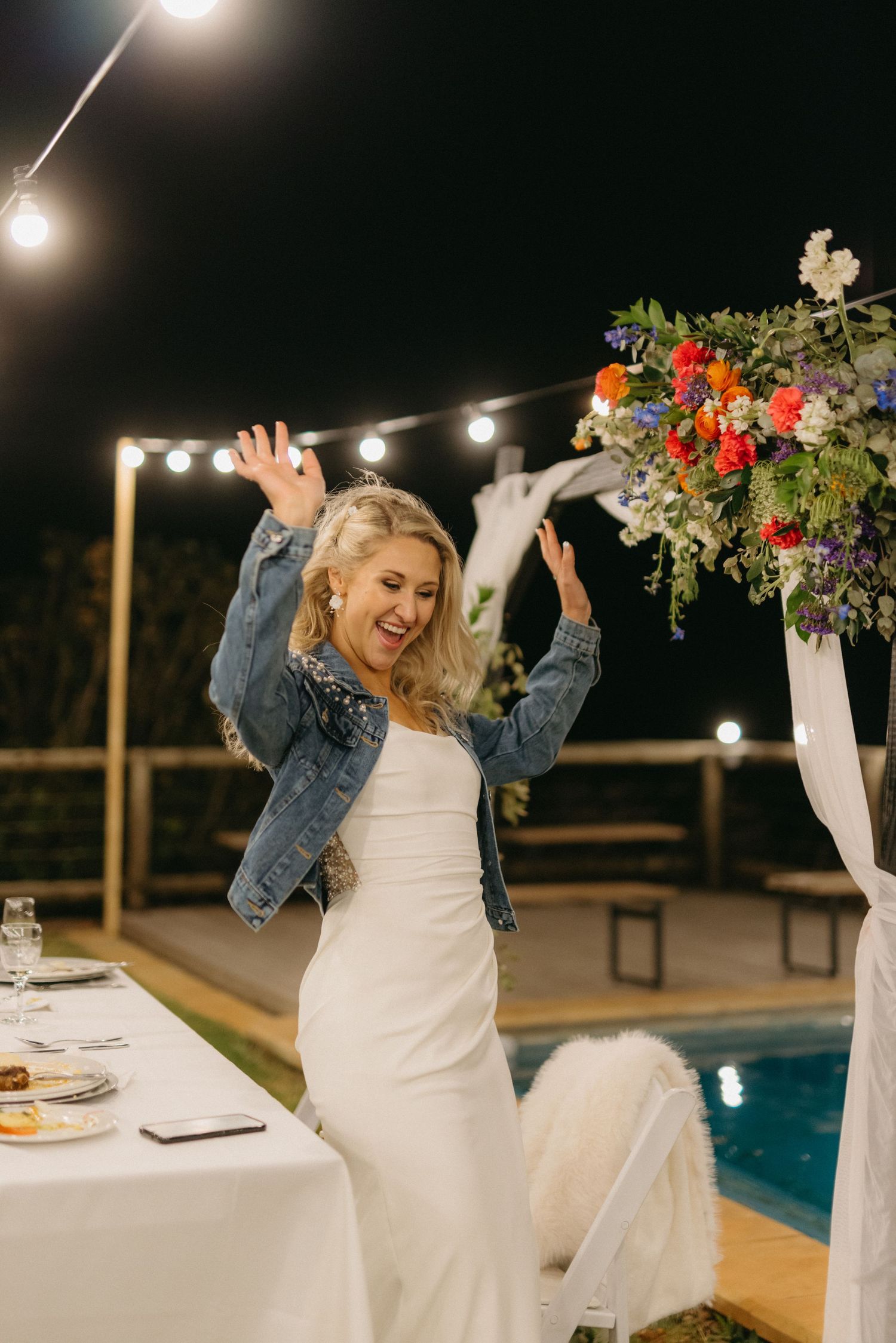 Wedding celebration by a pool at night with string lights and floral decorations creating an intimate atmosphere.