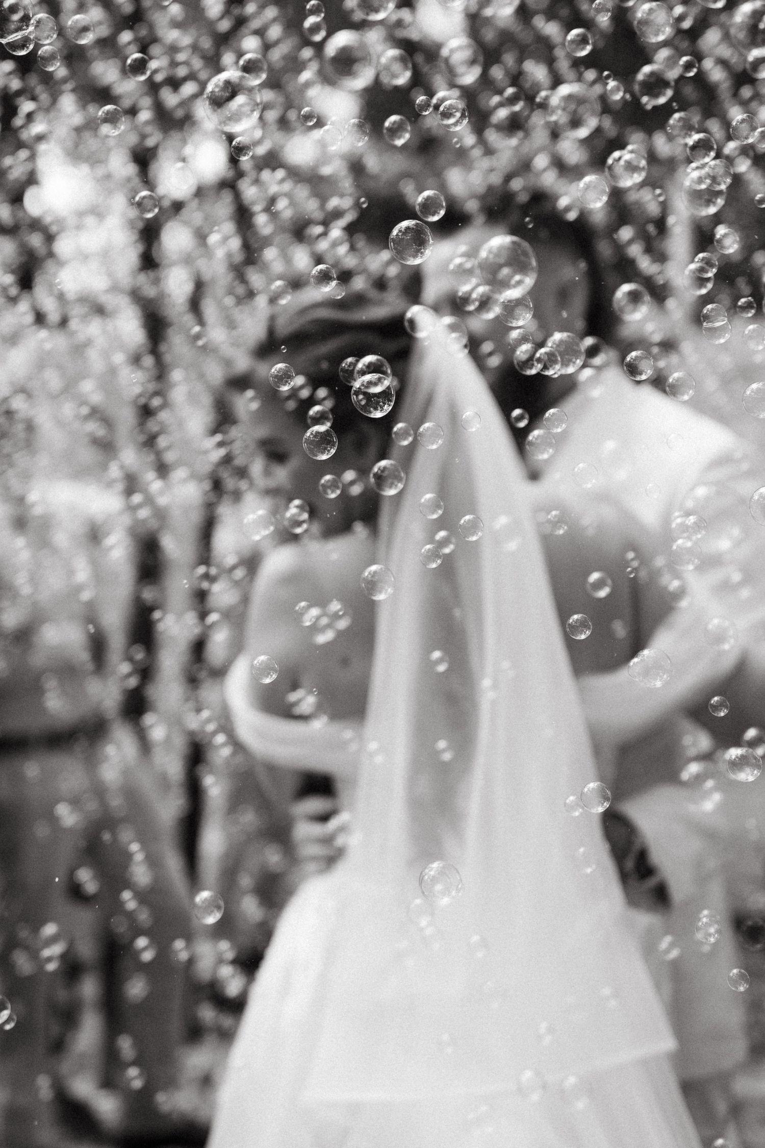 A dreamy black and white wedding photo with soap bubbles floating around a bride in her white veil and gown.
