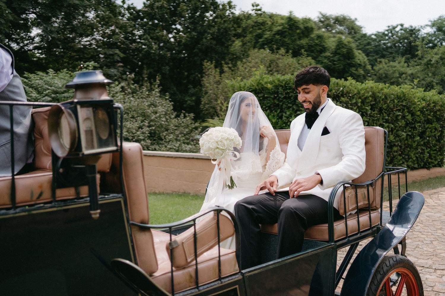 A couple riding in a horse-drawn carriage through a lush garden setting at their wedding.