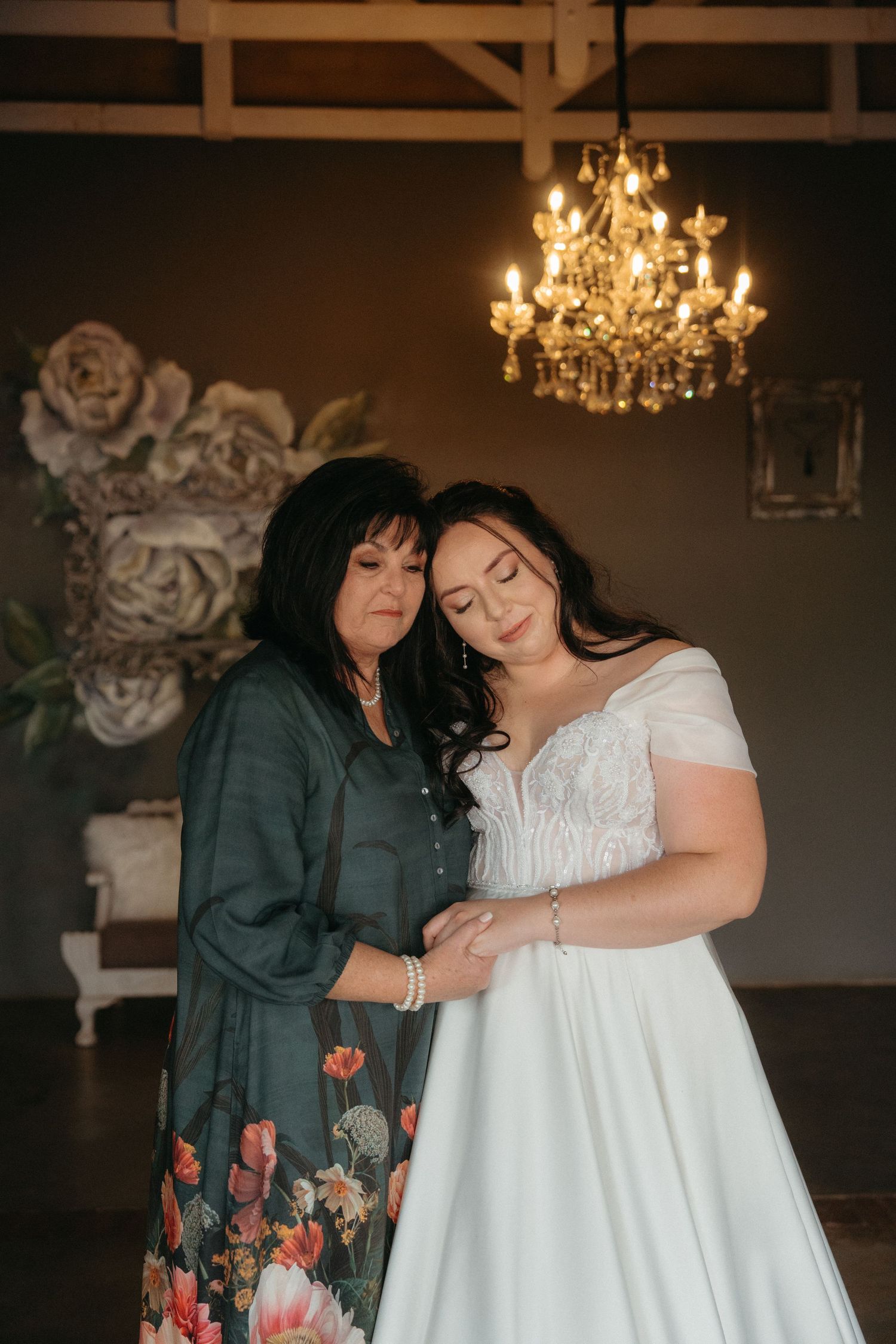 A tender moment in a wedding venue with a crystal chandelier and floral wall decor.