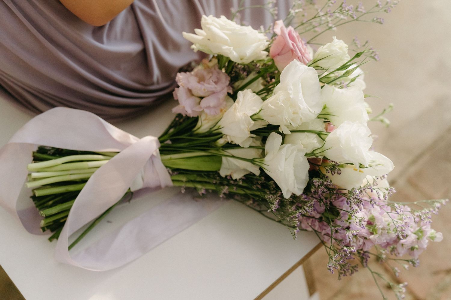 An elegant bridal bouquet with white and pink flowers wrapped in satin ribbon laying on soft fabric.