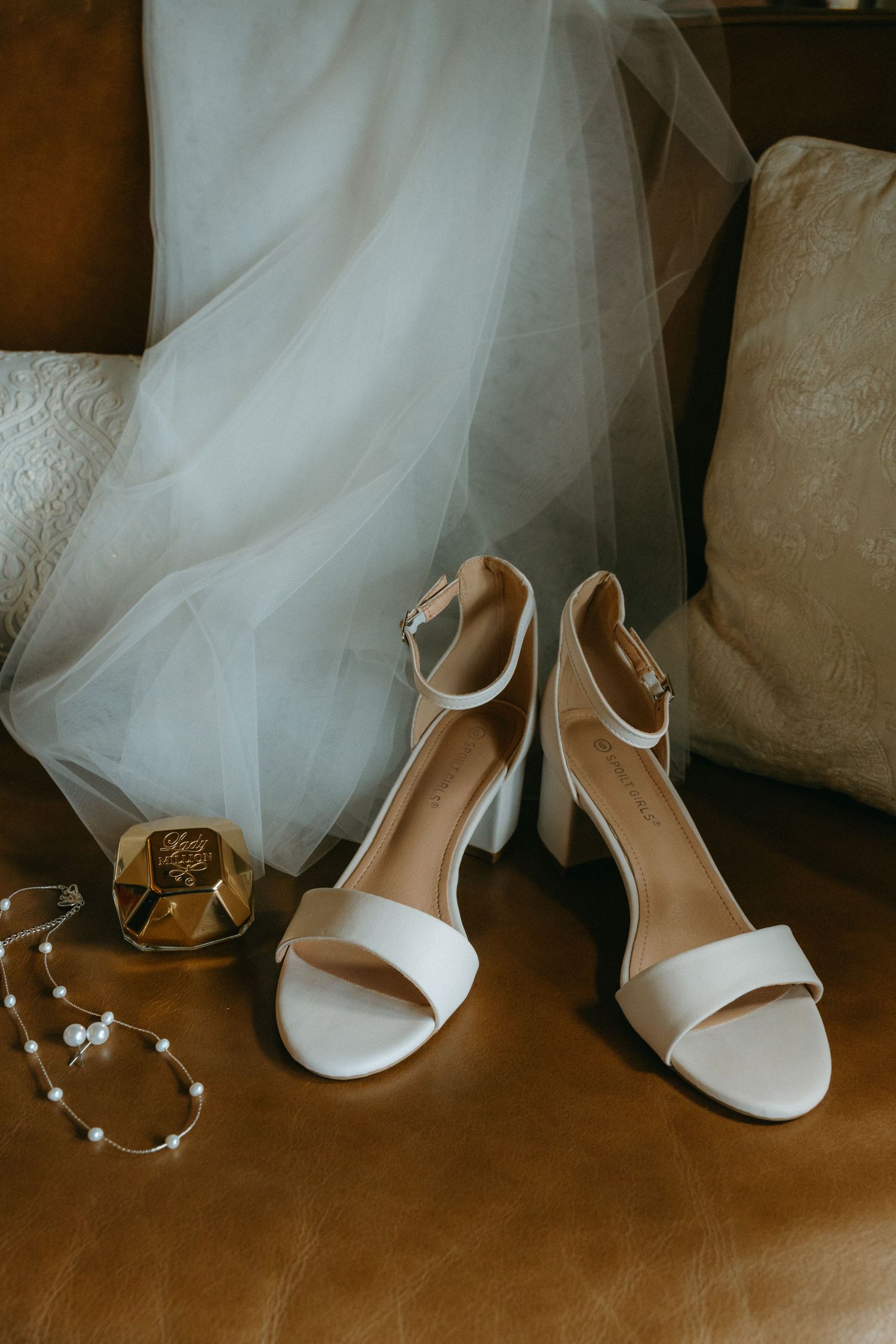White bridal shoes and delicate jewelry displayed against tulle wedding dress.