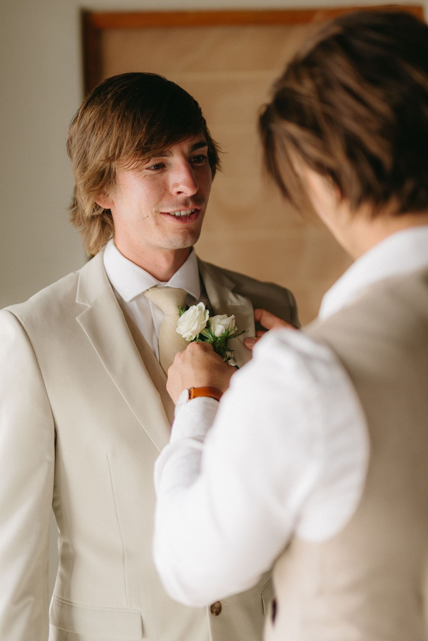 Wedding preparation moments with white formal attire and floral boutonniere.