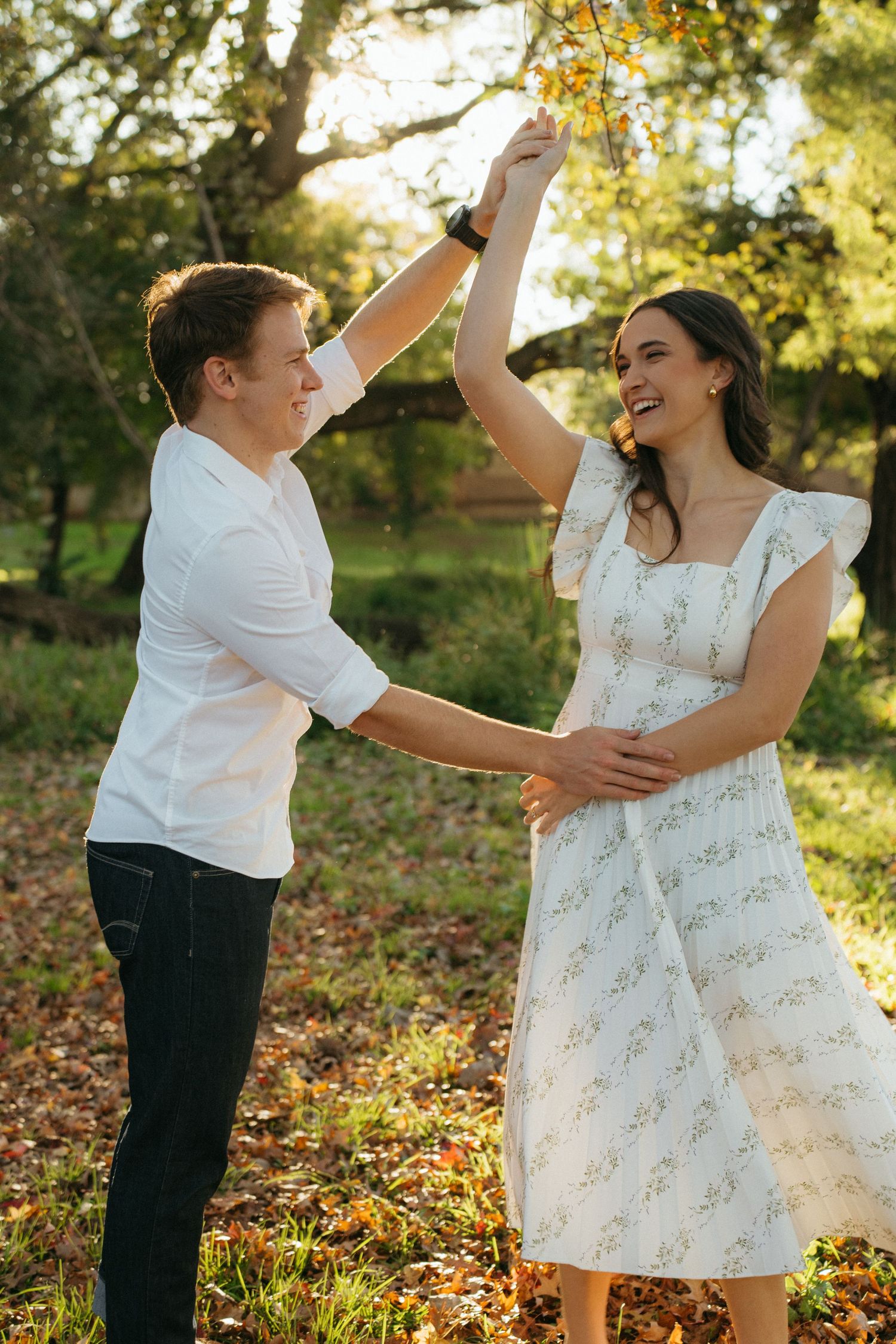 Couple dancing and laughing together in autumn sunlight with leaves falling in a garden setting.