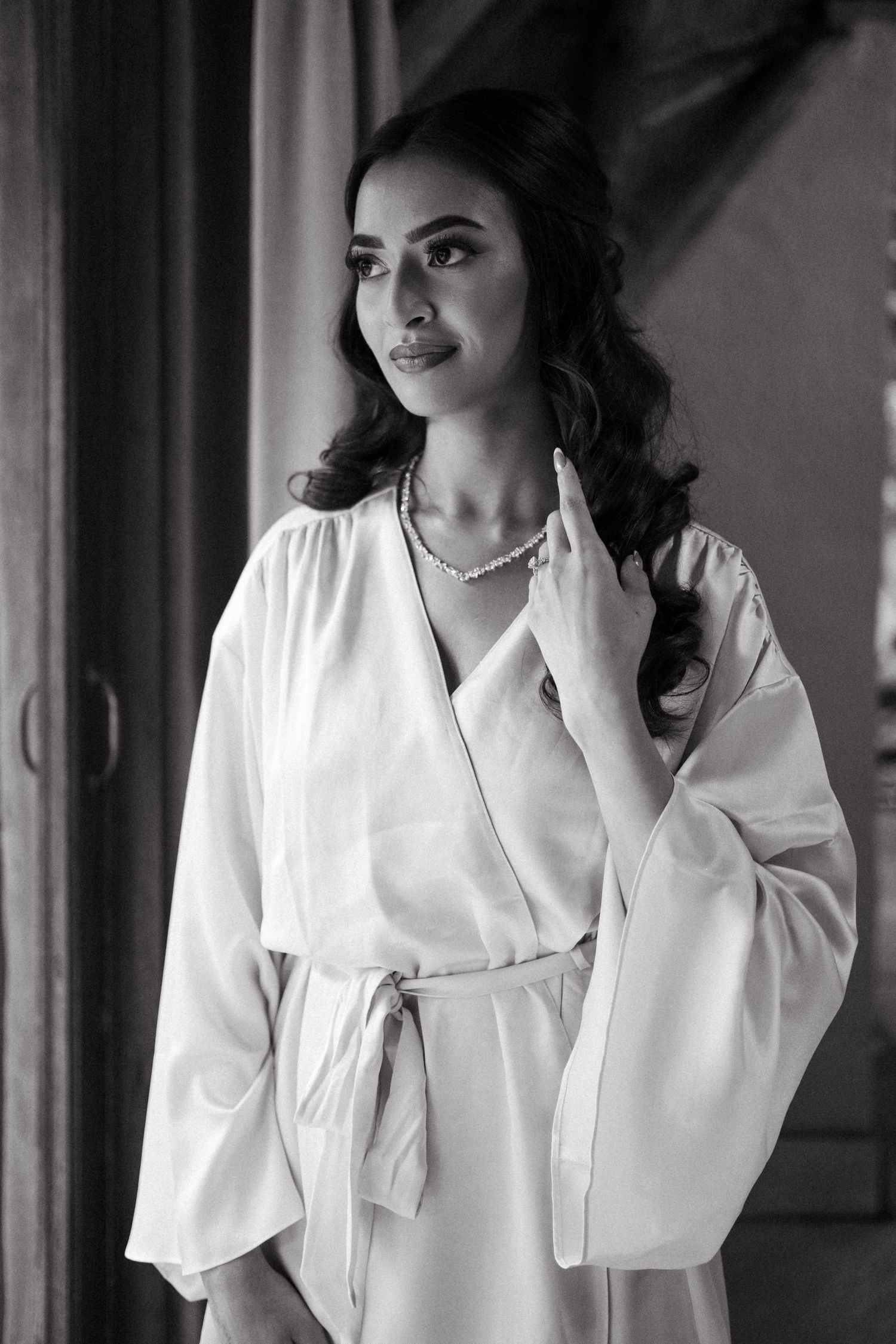Black and white portrait of woman in white silk robe with elegant jewelry and wavy hair.
