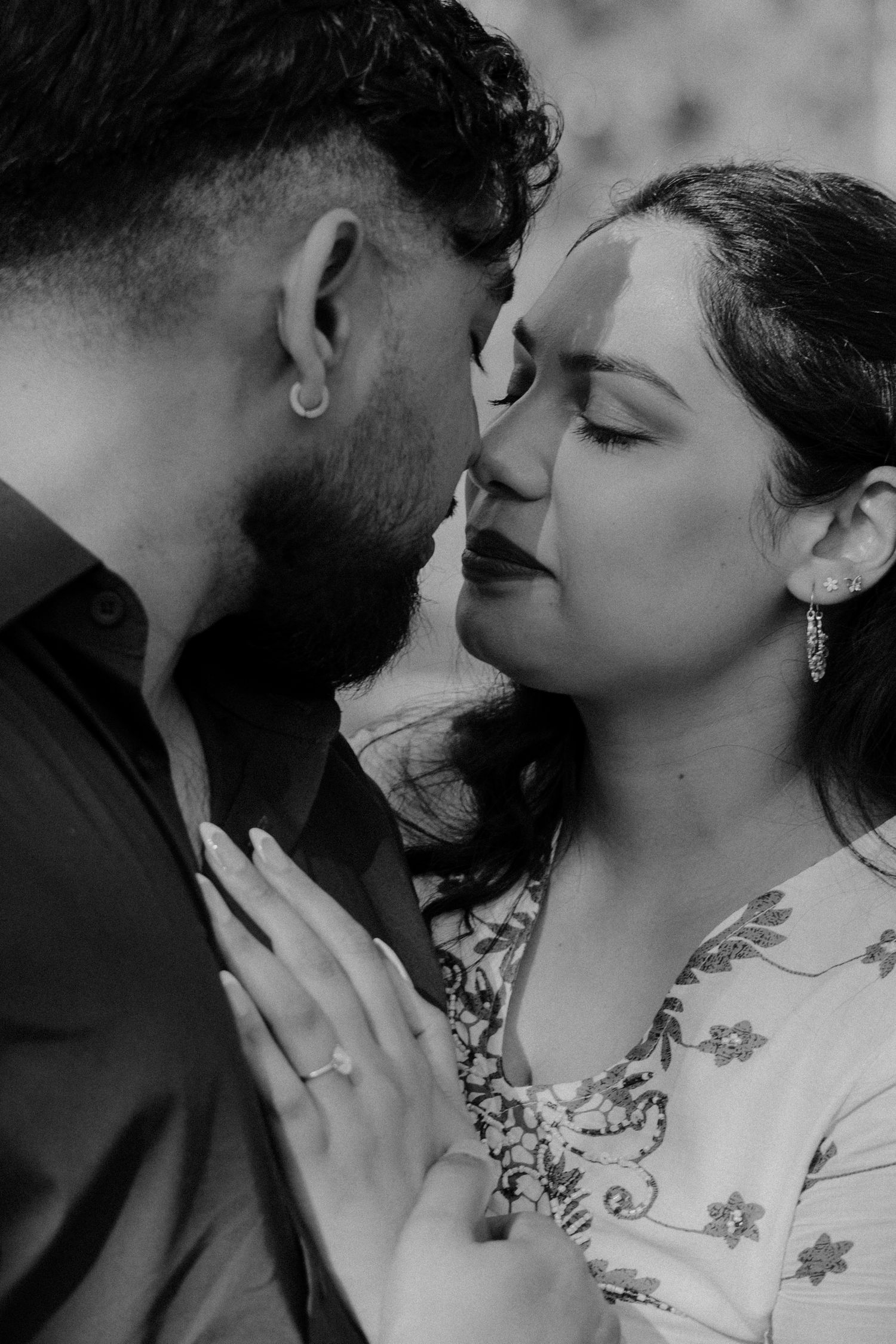 Intimate black and white portrait of couple in close embrace with her wearing floral dress and him in dark shirt.