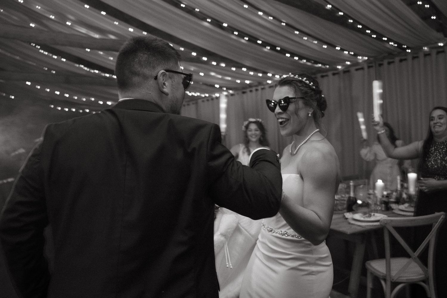 String lights illuminate a wedding reception dance floor as guests celebrate and dance together.