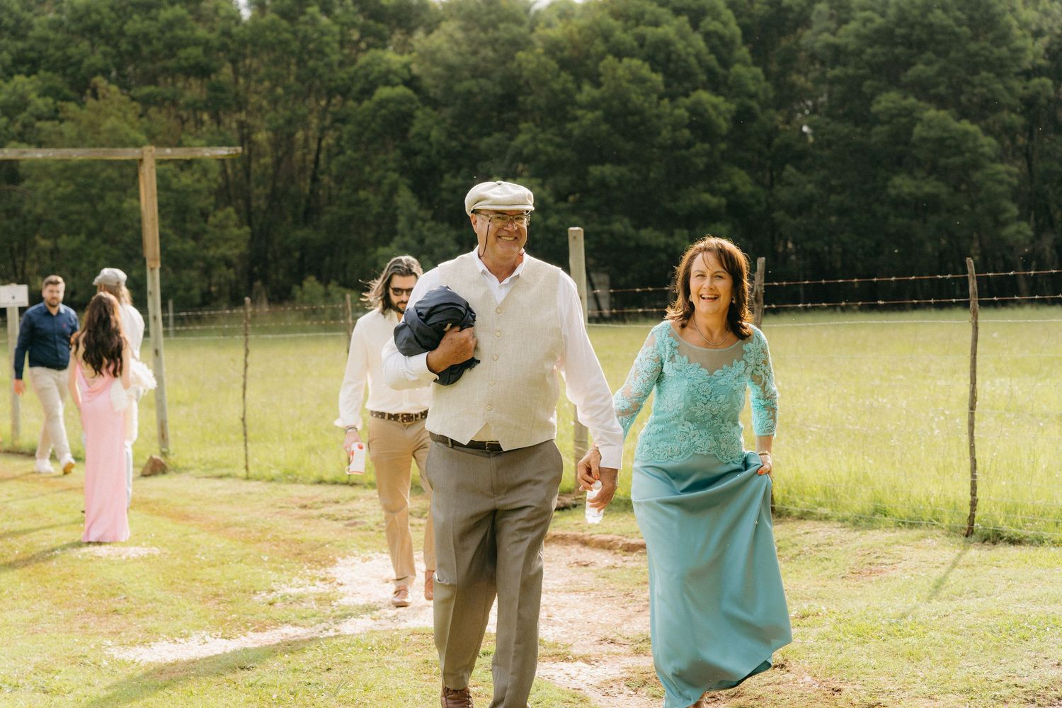 Wedding guests walking across a sunny field during outdoor celebration.