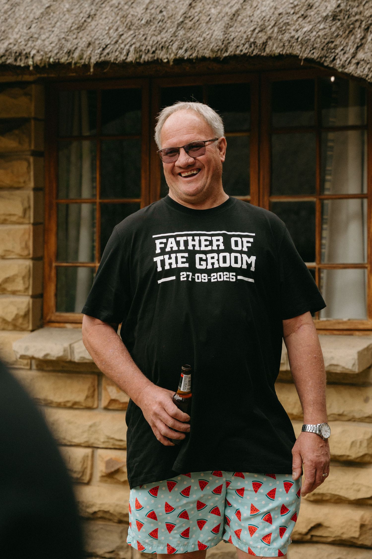 Someone wearing a 'Father of the Groom' t-shirt and festive patterned shorts at a wedding celebration.