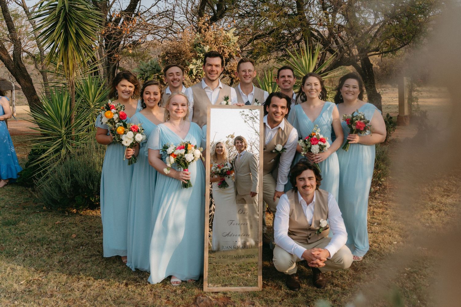 Wedding party poses together in coordinated blue and white attire against natural outdoor backdrop.