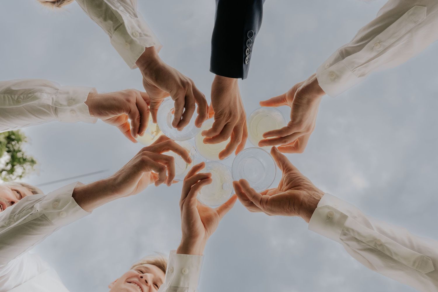Multiple hands reach toward each other against a bright sky background.