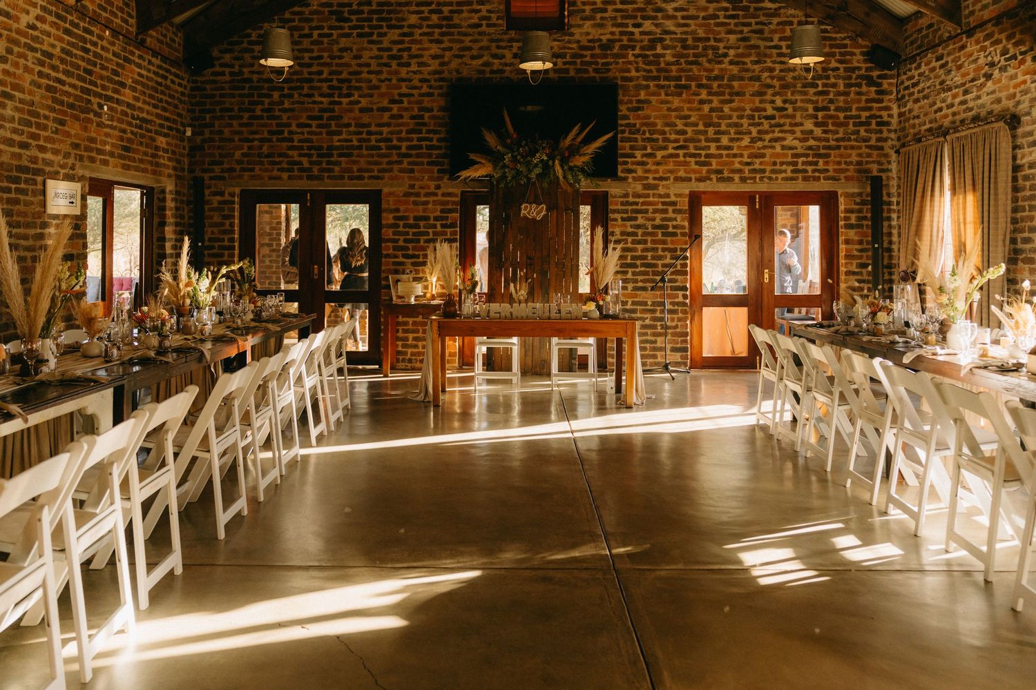Interior of a rustic brick venue with elegant lighting and white chairs set up for a reception.