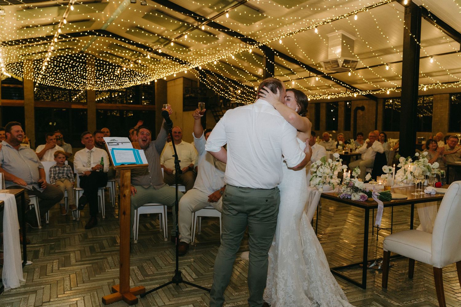 Couple sharing their first dance under twinkling lights at indoor reception venue.