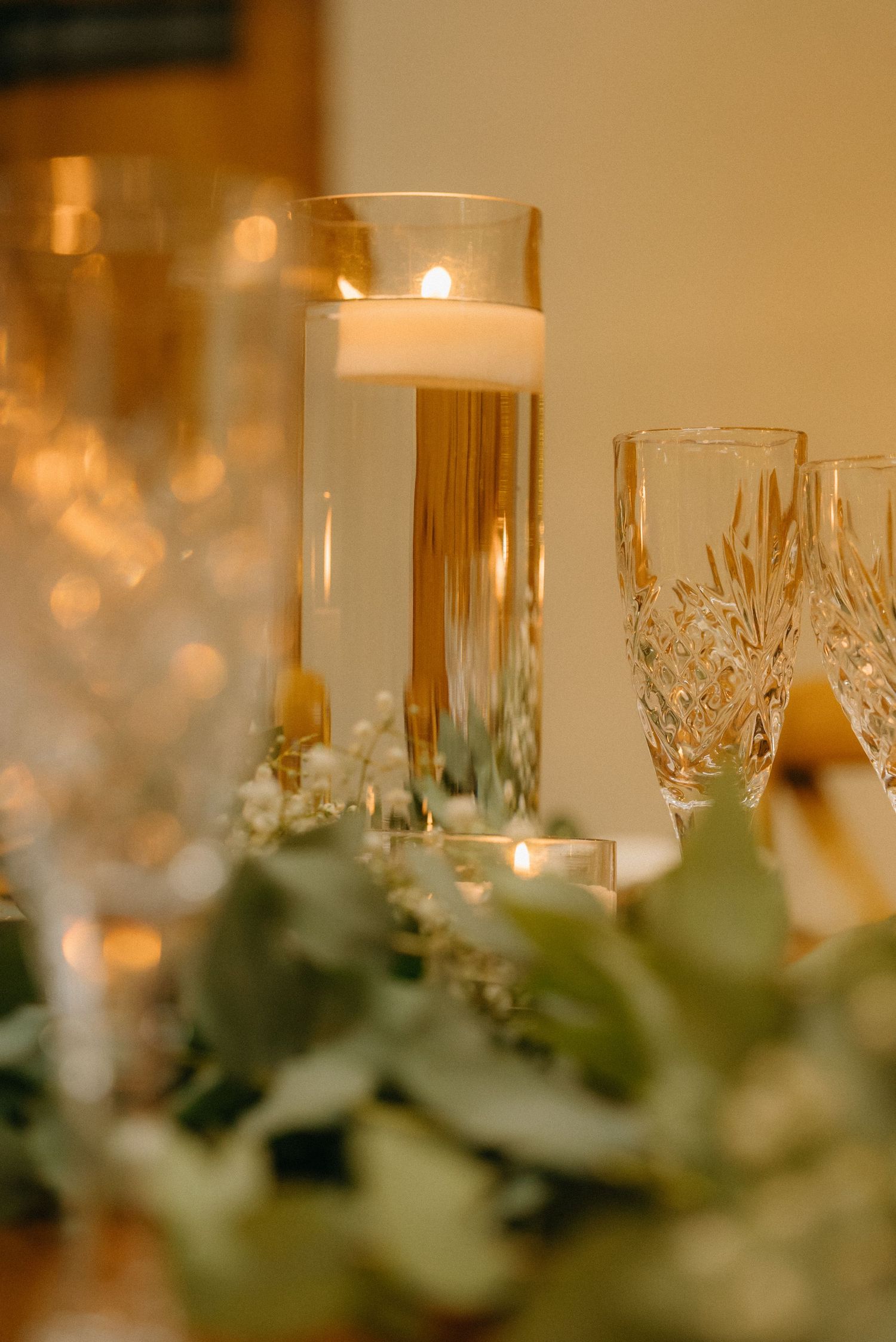 Crystal glasses and greenery create an elegant table setting with warm candlelight.