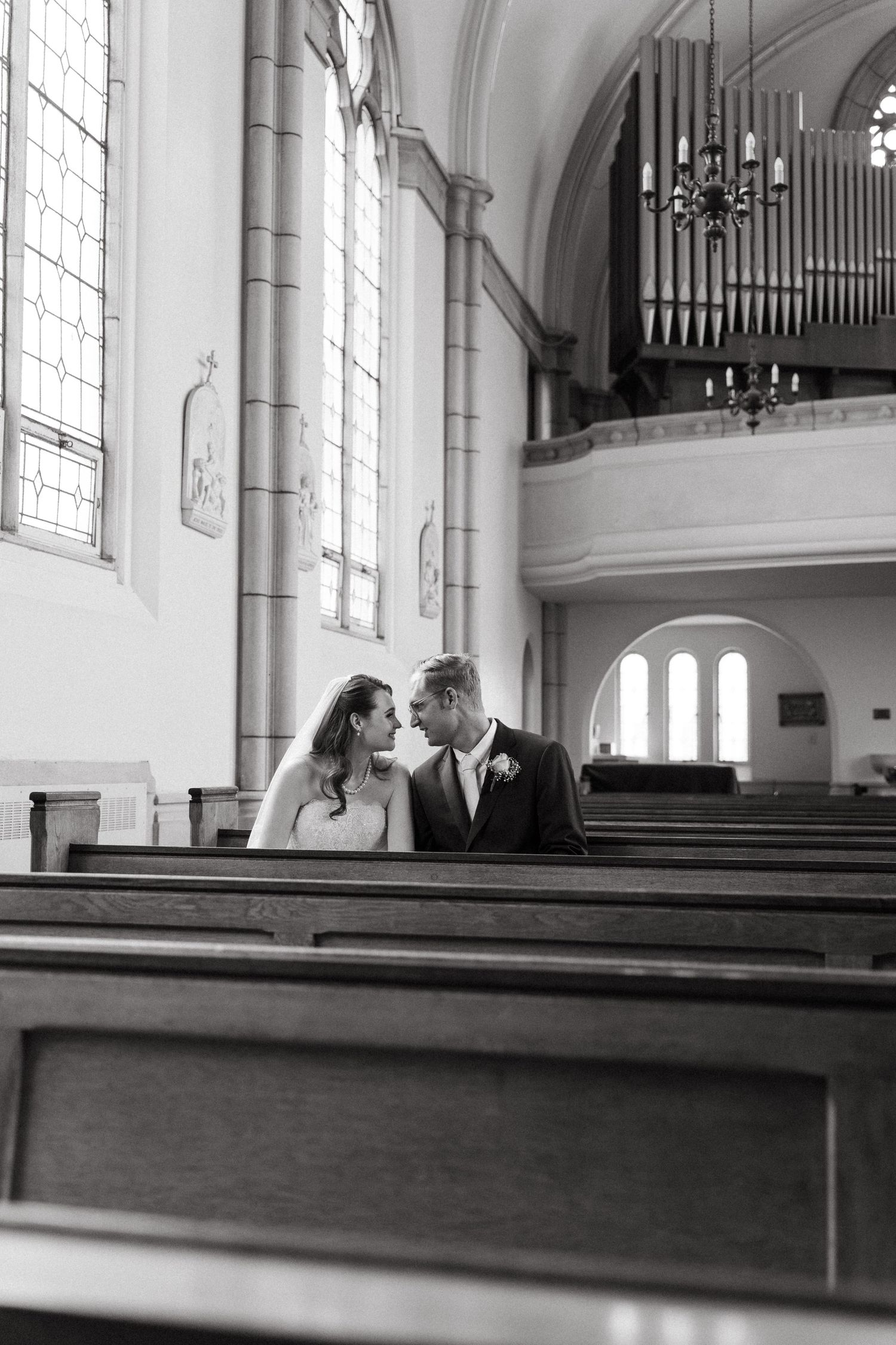 A romantic black and white photograph of a couple sharing an intimate moment in a church pew with organ pipes visible above.