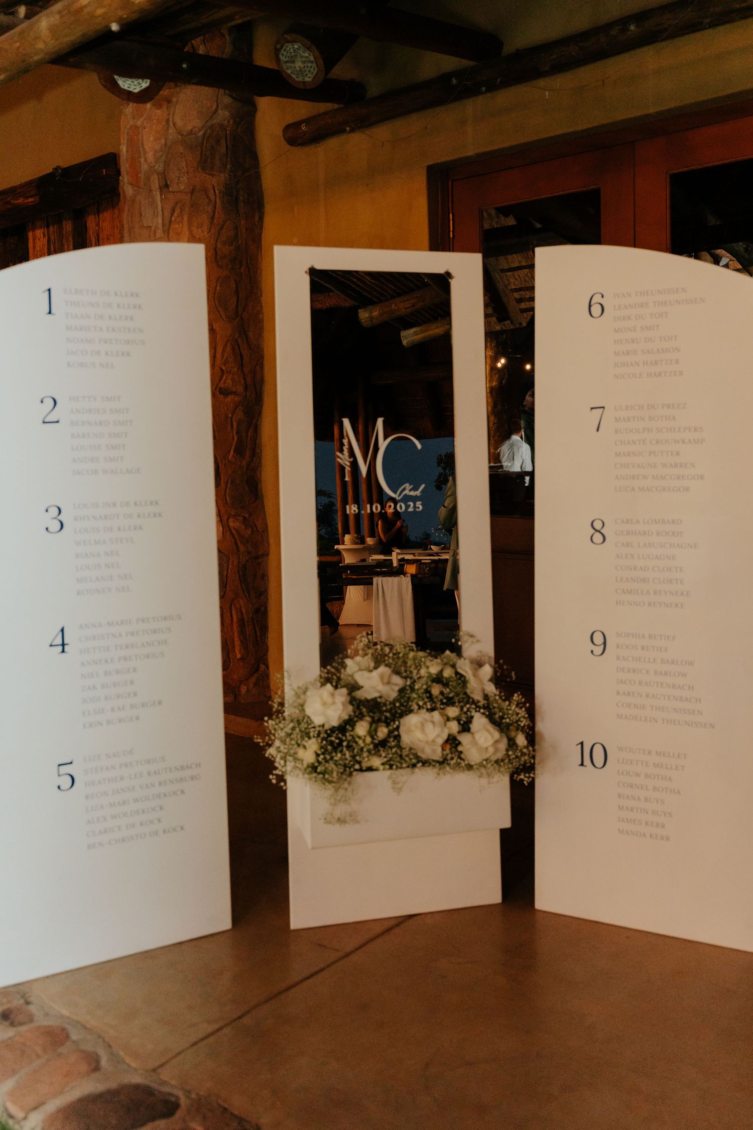 Wedding seating chart display with numbered cards arranged on rustic wooden beams.