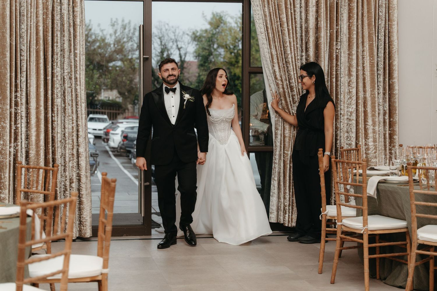 Bride and groom make grand entrance at elegant wedding reception venue with gold curtains and Chiavari chairs.