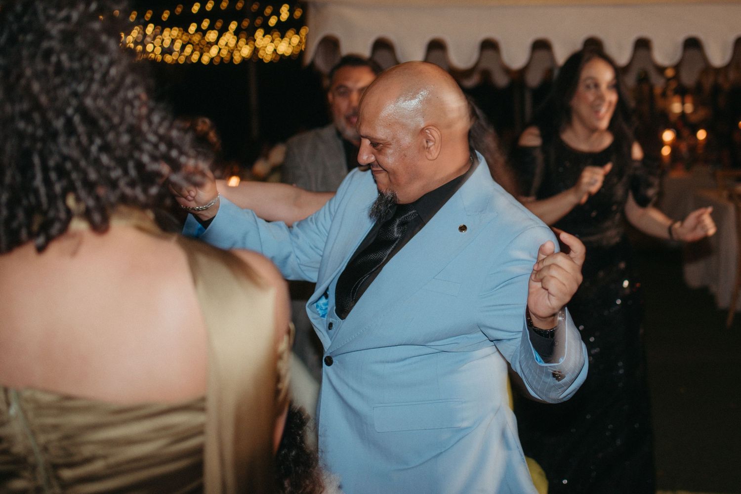 Elderly man in light blue suit dancing joyfully at an elegant evening reception party.