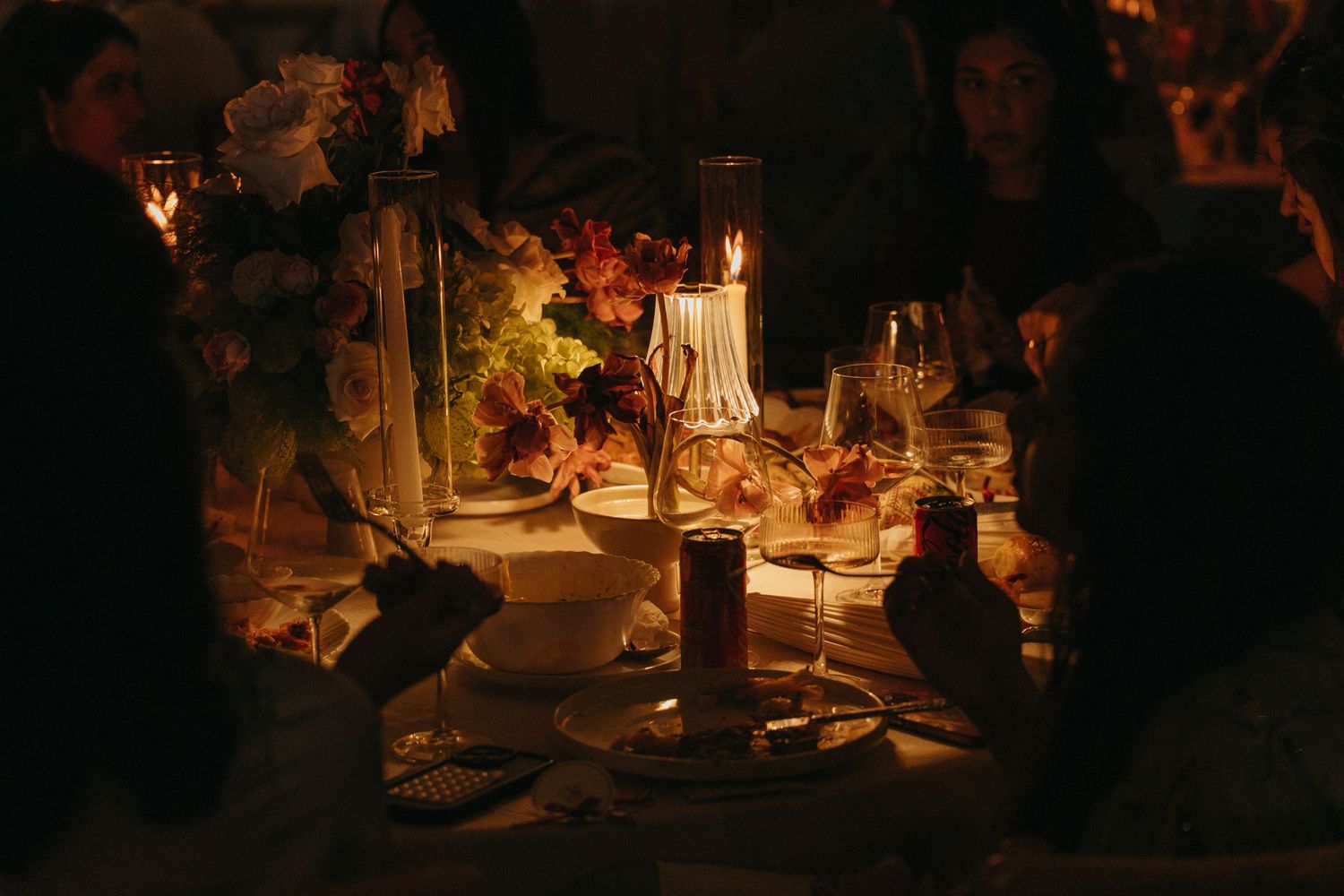 Guests gathered around a candlelit dinner table with floral arrangements and glowing candles in a warm, dimly lit setting.