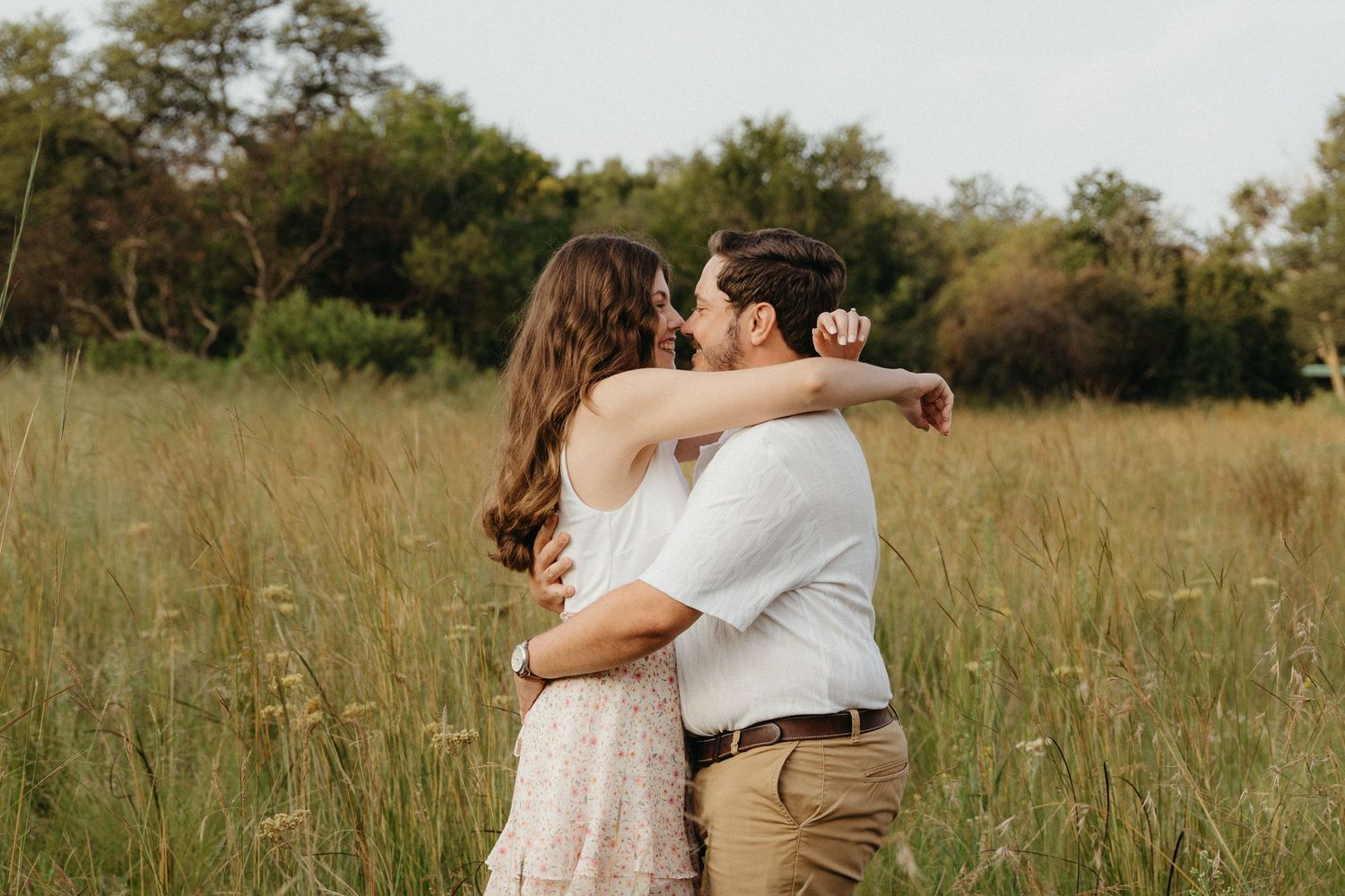 Couple embracing and kissing in a lush green meadow field, romantic outdoor engagement photo.