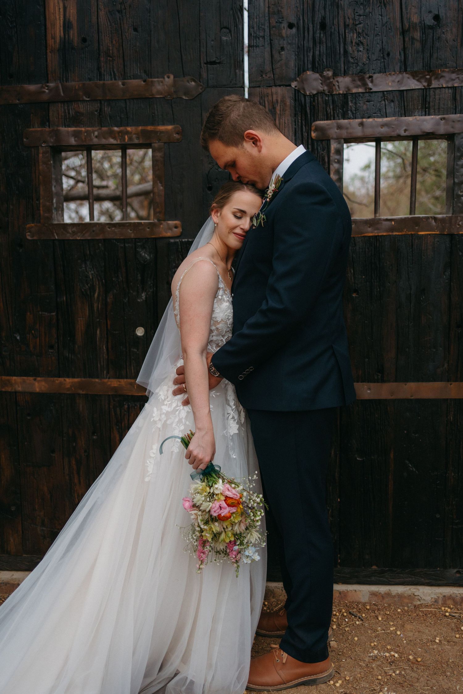 Intimate wedding portrait against a rustic wooden backdrop with a colorful bouquet.