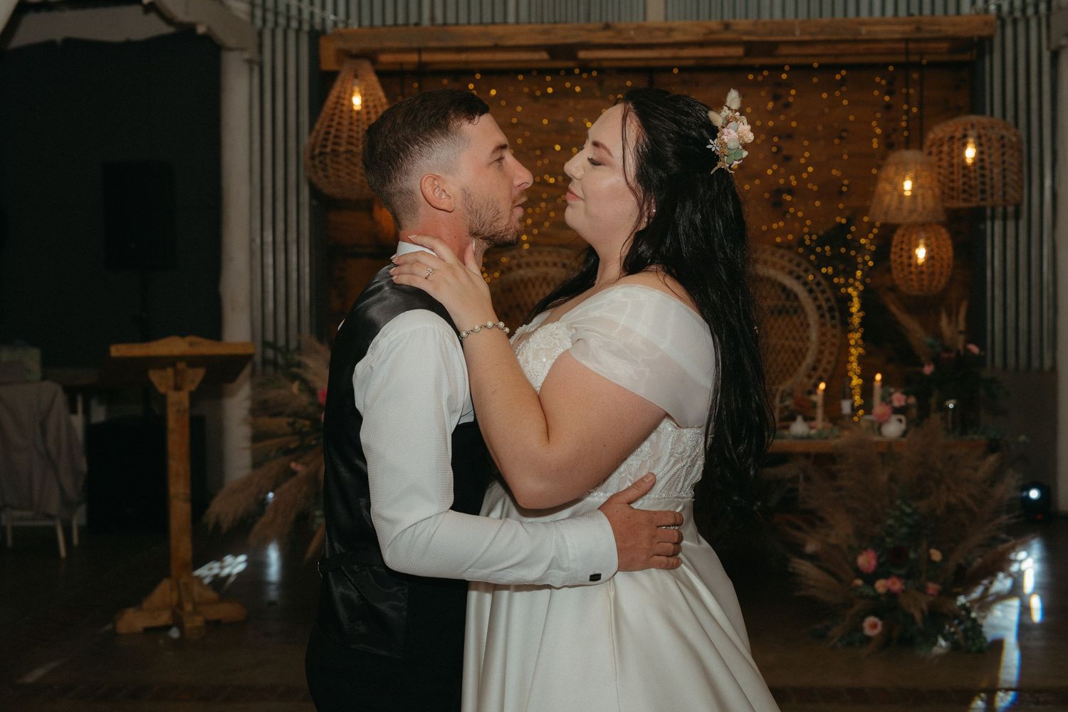 A couple shares a romantic dance moment at their wedding reception with warm lighting and elegant decor in the background.