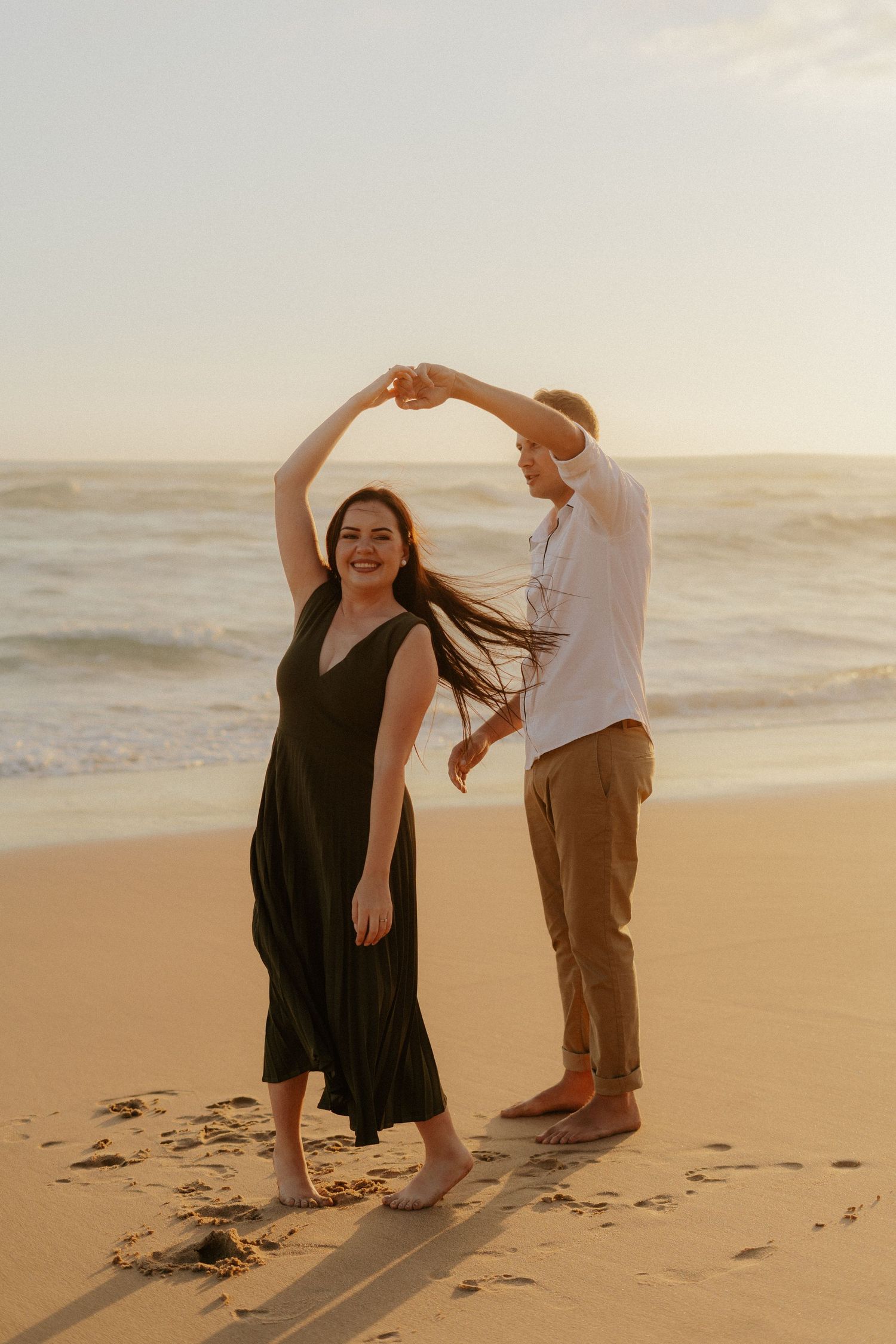 A couple dancing together on a sandy beach at sunset for their Western Cape engagement photo shoot