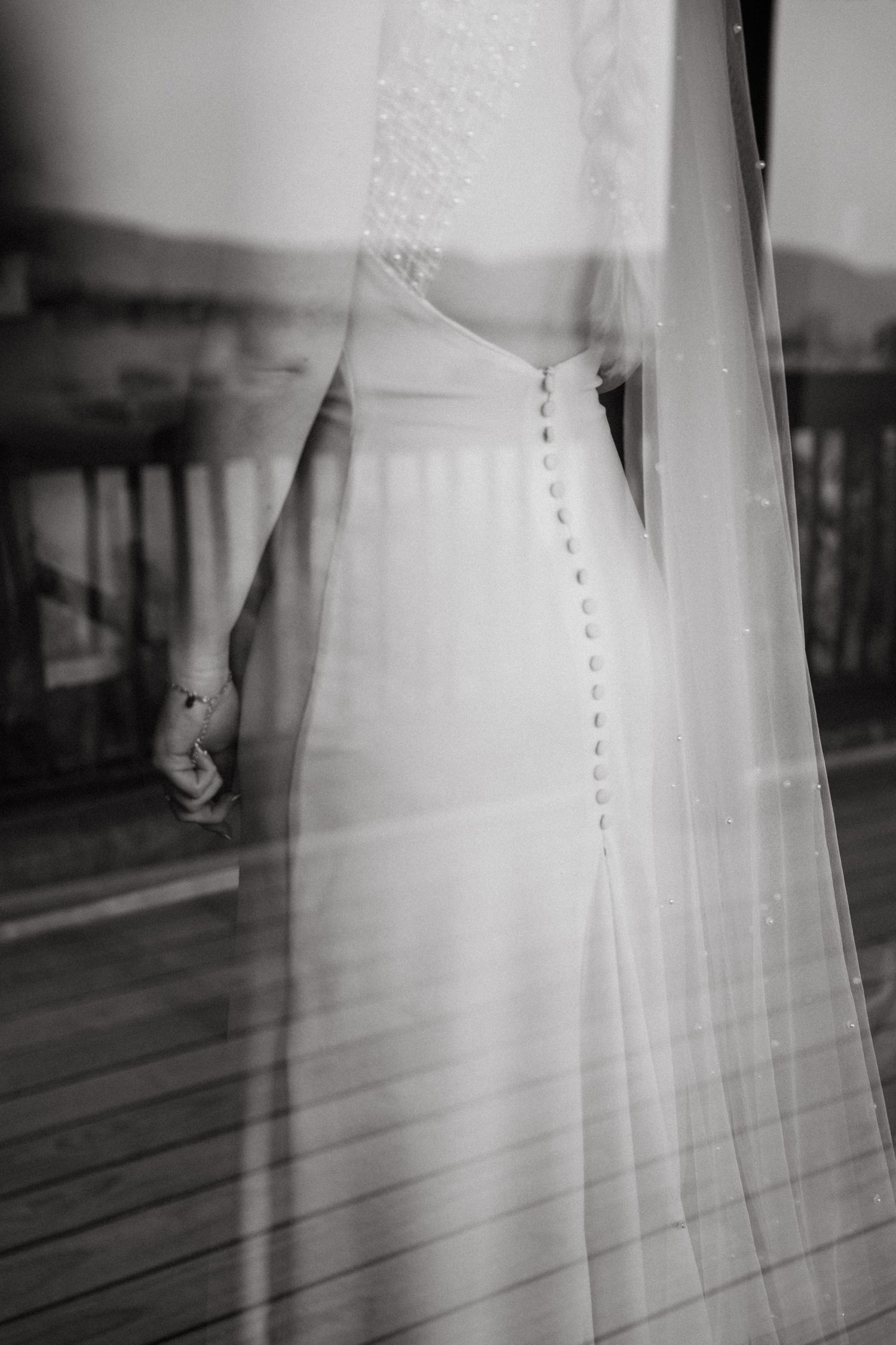 Close-up detail shot of a wedding dress buttons and flowing veil in black and white.