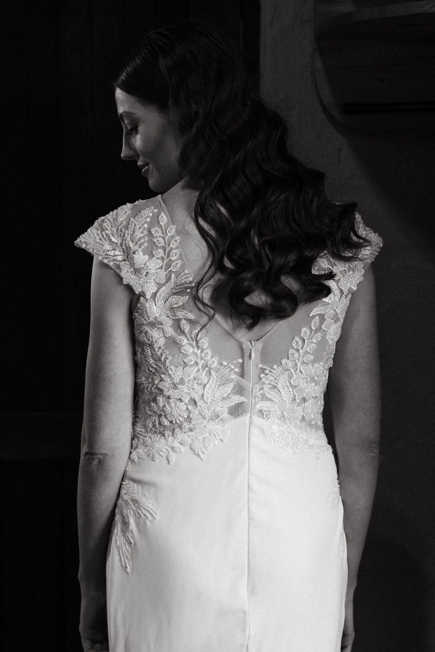 Back view of an elegant lace wedding dress showing intricate detail and flowing curled hairstyle.