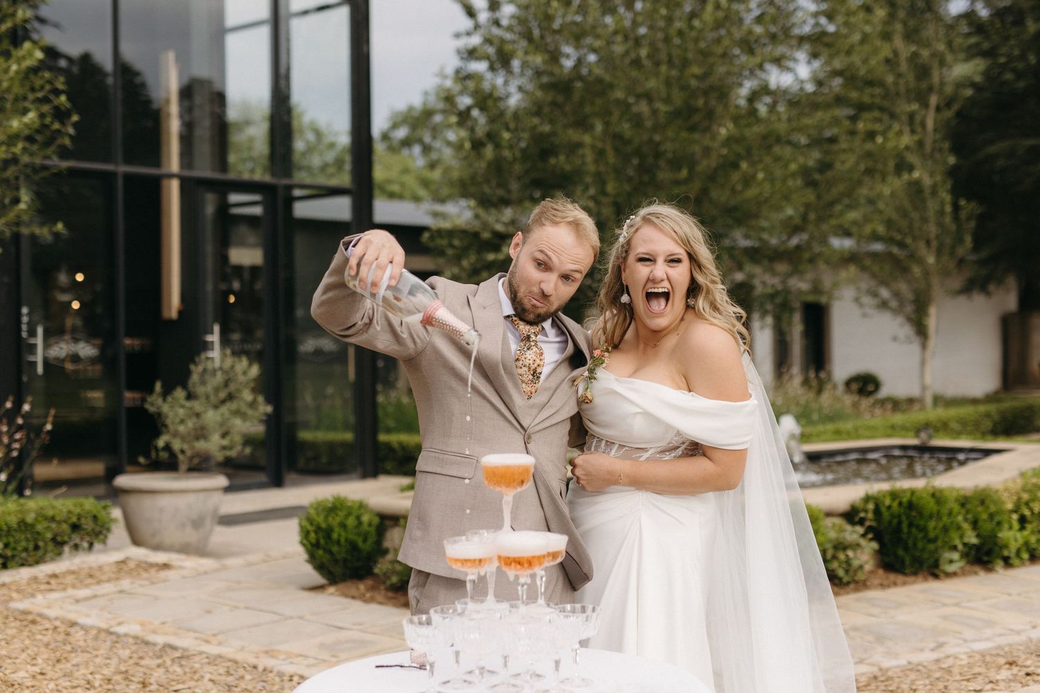 Wedding celebration moment as couple pours champagne into tower of glasses outdoors.