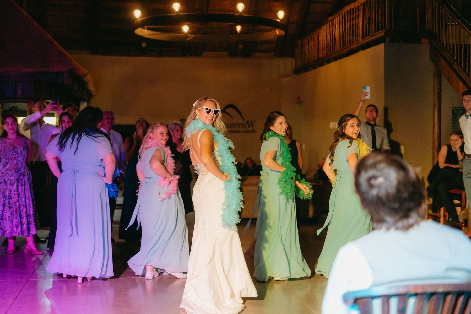 Wedding party dancing on the dance floor illuminated by purple and pink lighting at an evening reception celebration.