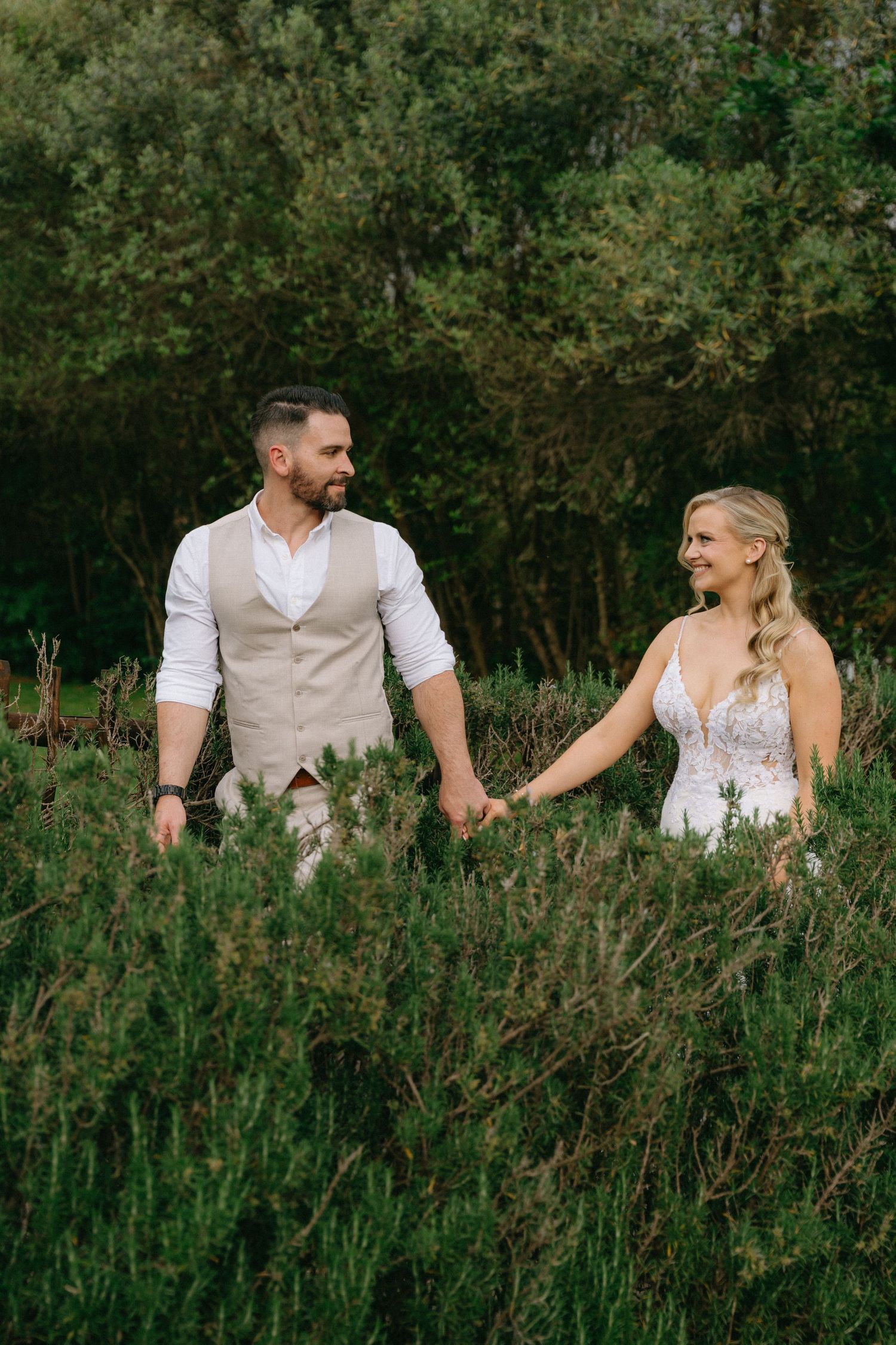 A couple poses together in tall grass and wildflowers during an outdoor photo session.