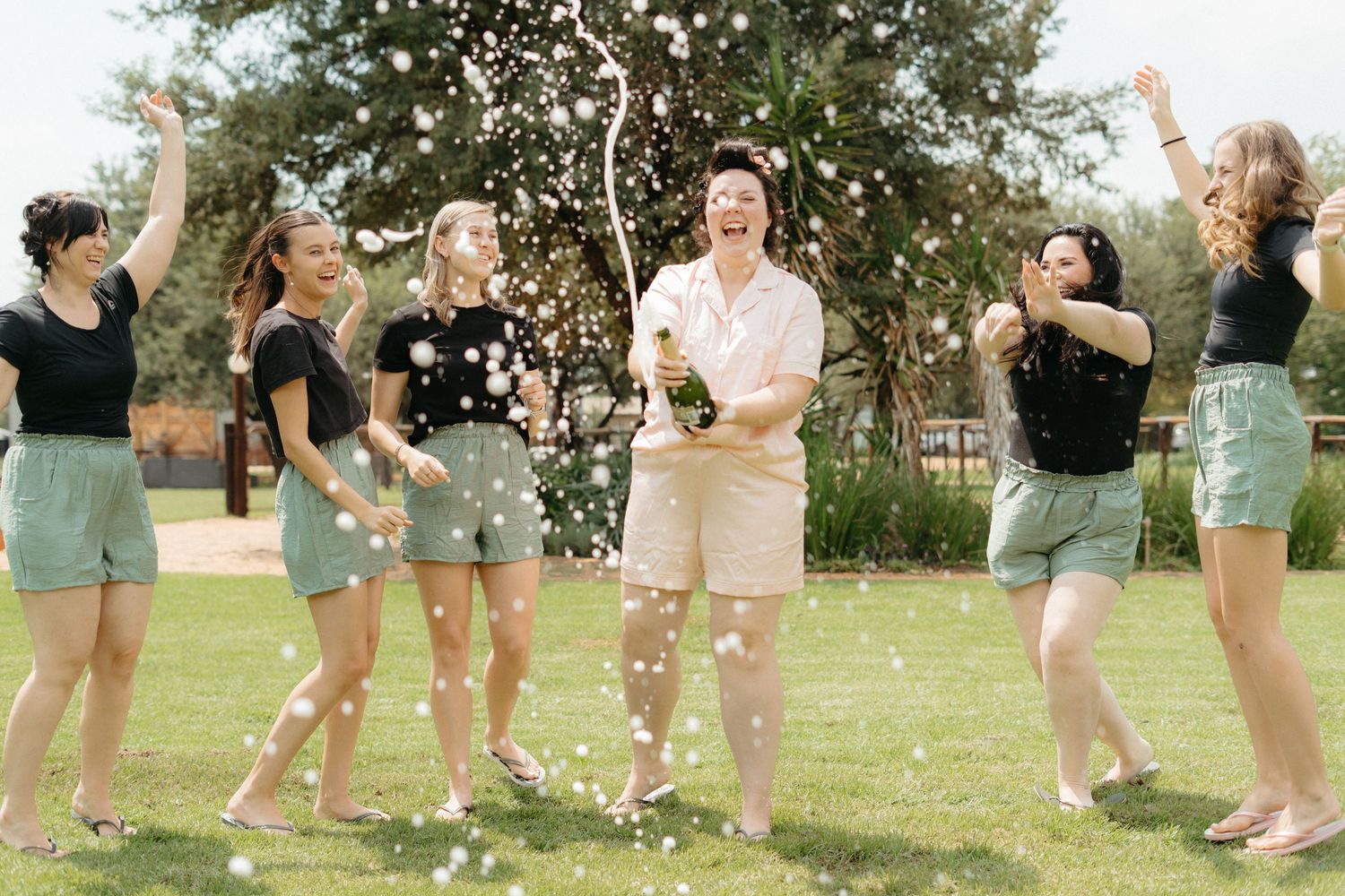 Group of friends in matching outfits celebrating with confetti in an outdoor garden setting.