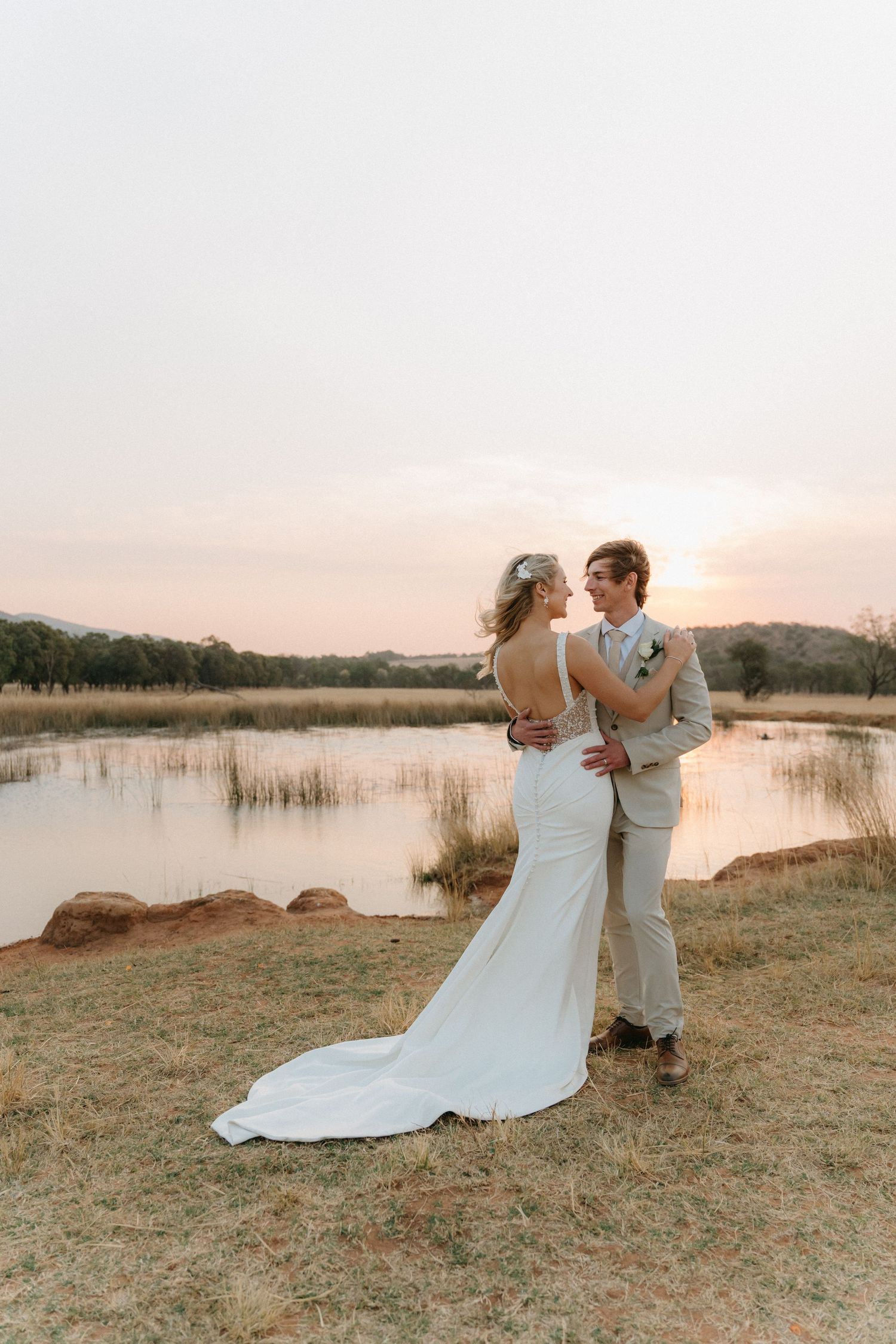 Romantic wedding couple dances together by a lake during sunset.