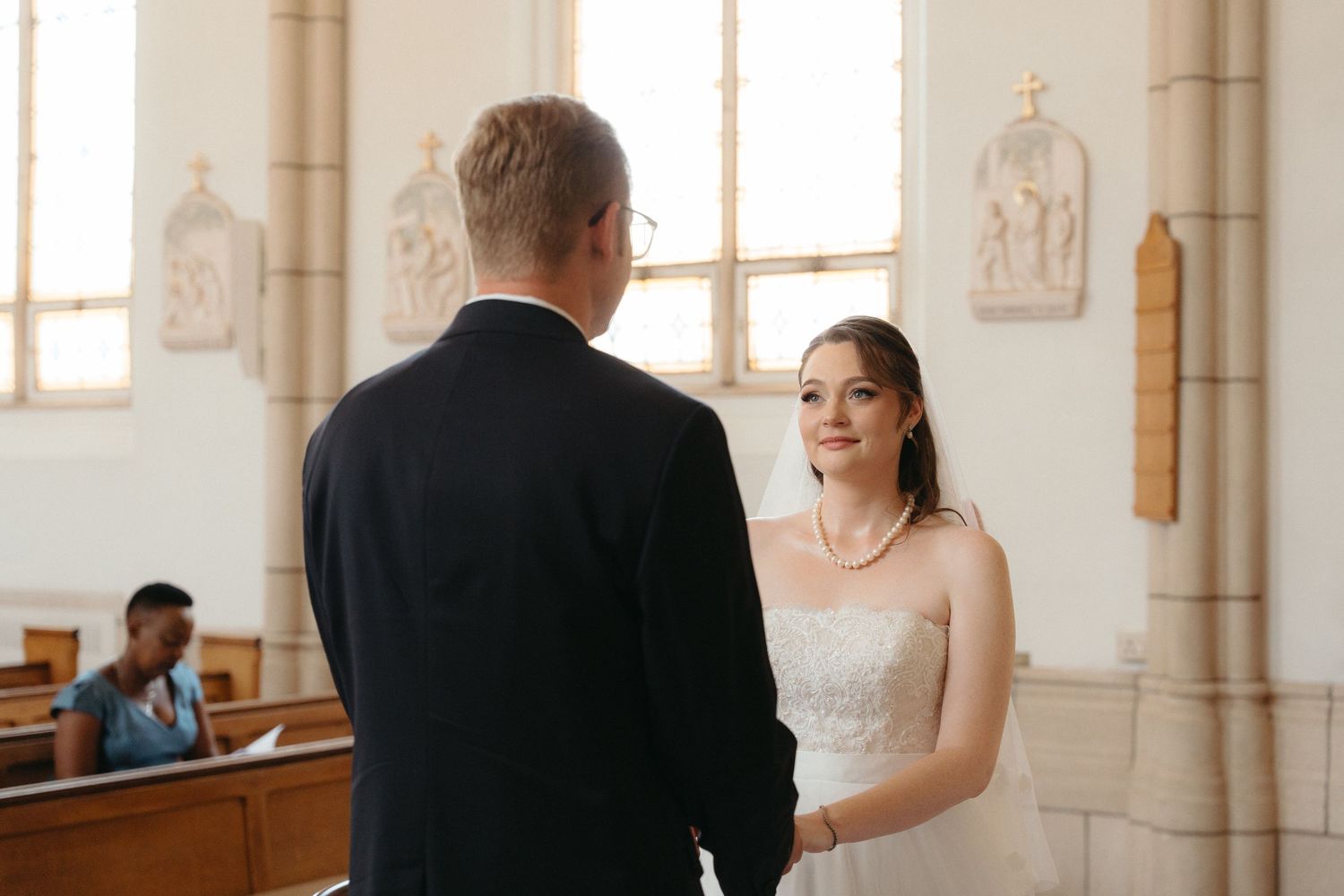 A bride and groom share an intimate moment during their wedding ceremony in a bright, elegant church interior.